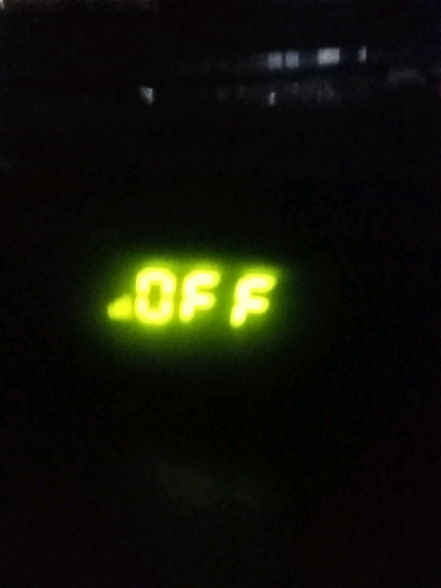 A close-up, low-light image displays a bright green digital display with the text ".OF" illuminated against a dark background. The text is slightly blurred, suggesting it is either in motion or the camera is out of focus. The overall scene is dark, with some faint, out-of-focus lights visible in the upper portion of the image, which may indicate a dimly lit environment like a car interior or a night-time setting. There is no discernible information about the location in Kebonagung, Indonesia, or any specific context beyond the illuminated text.