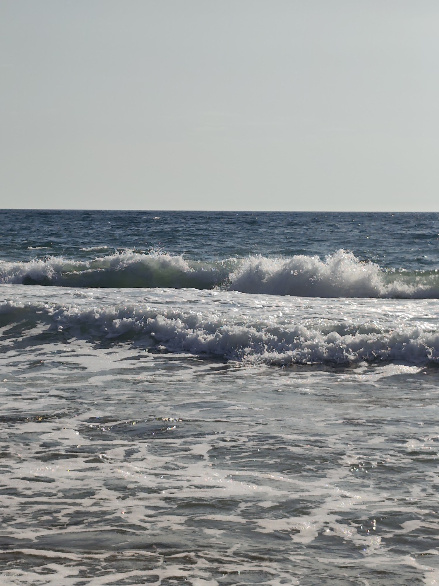 The image shows a body of water with waves. The water is a deep blue and the waves are white with foam. The sky is a pale gray and there is no sun visible. The scene is serene and peaceful. The image is not specific to Saiyn, Kazakhstan and provides no information about this location.
