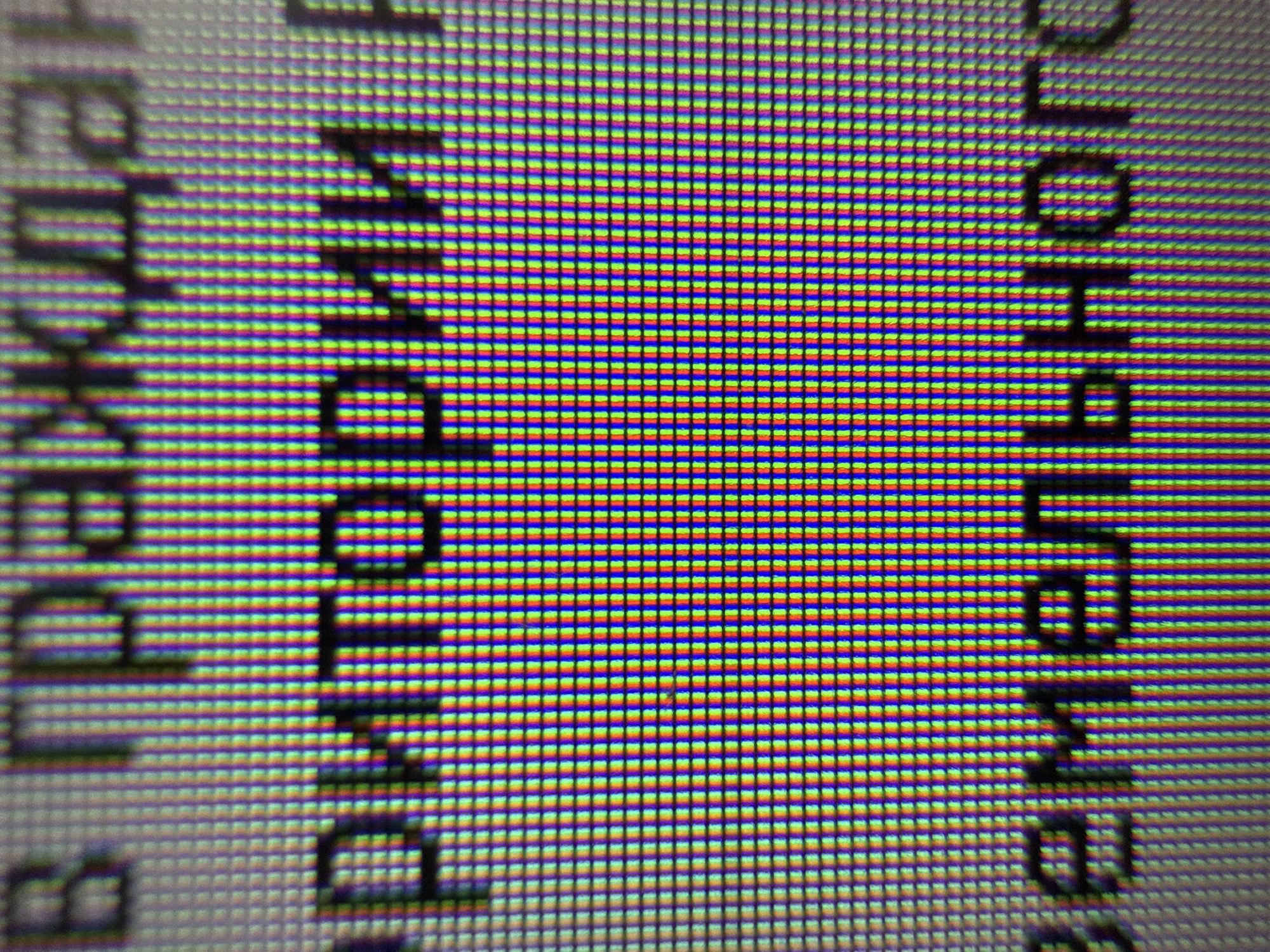 The image shows a close-up view of a screen displaying text. The pixel structure of the screen is visible, with individual red, green, and blue subpixels arranged in a grid pattern. The text appears blurred and fragmented due to the extreme magnification. Part of the word 'chaikovsky' and 'раздел' in Russian is visible, suggesting a digital interface possibly related to Chaikovsky, Russia.