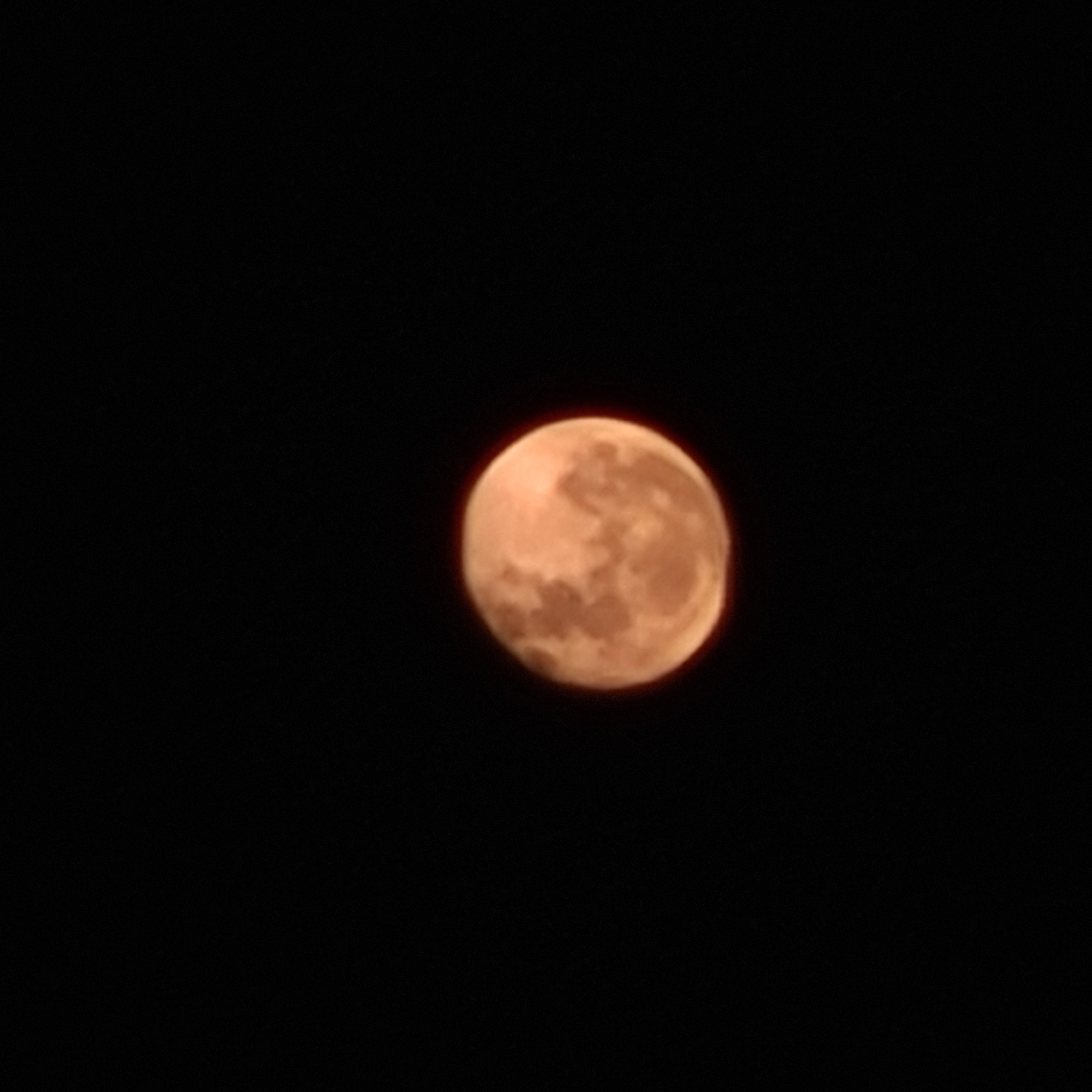 The image shows a full moon in the night sky. The moon has a reddish-orange hue and visible surface details. The background is completely black, indicating a night sky. The image does not provide any information about the location of the scene in the city of San Fernando del Valle de Catamarca, Argentina. There are no people, subjects, objects, actions, or interactions visible in the image other than the moon itself. The environment appears to be a clear night.