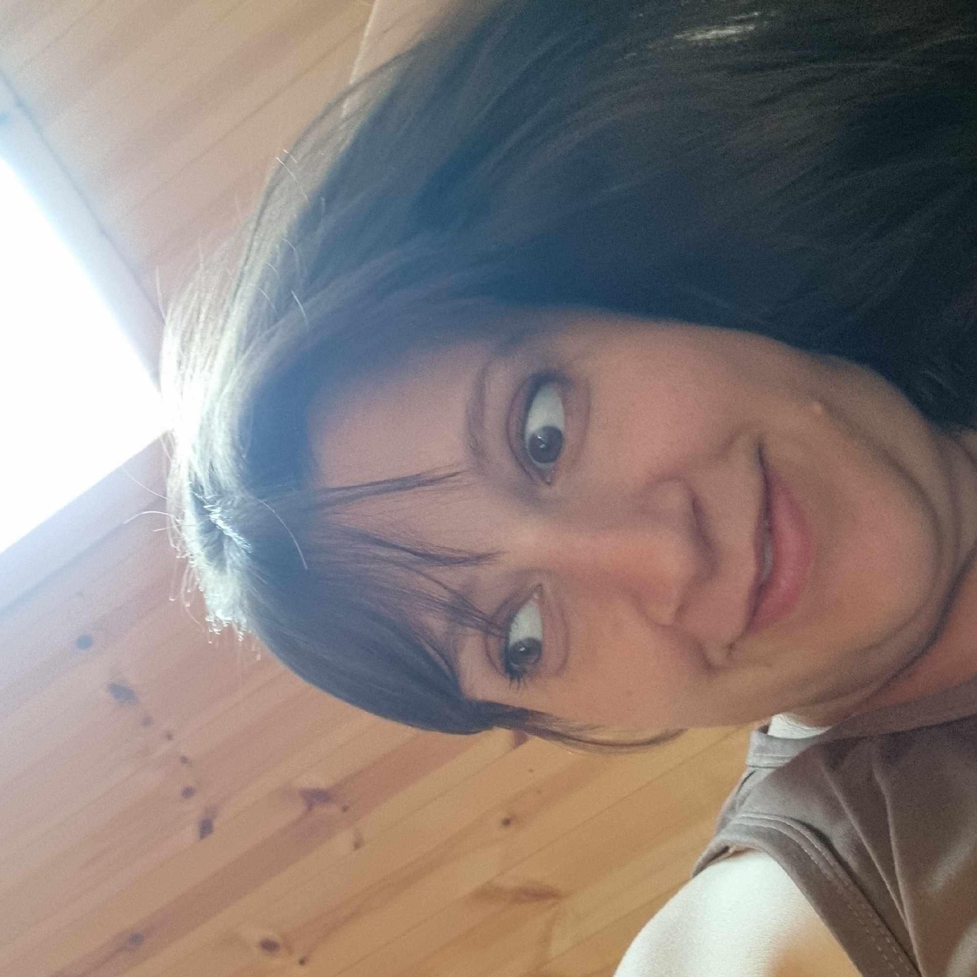 The image is a close-up, slightly tilted selfie of a woman. She is looking up and to the right, with her hair falling around her face. She is wearing a brown tank top. The background appears to be a wooden wall or ceiling. There is a bright light source in the upper right portion of the image. The specific location of Dunnae-myeon, South Korea is not depicted or suggested by the visual information in the image.