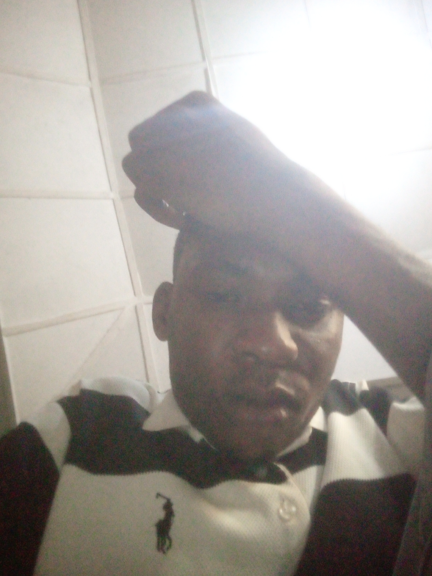 A person is holding their hand to their forehead. They are wearing a black and white striped collared shirt. The background appears to be a ceiling with square panels. The location is unknown.