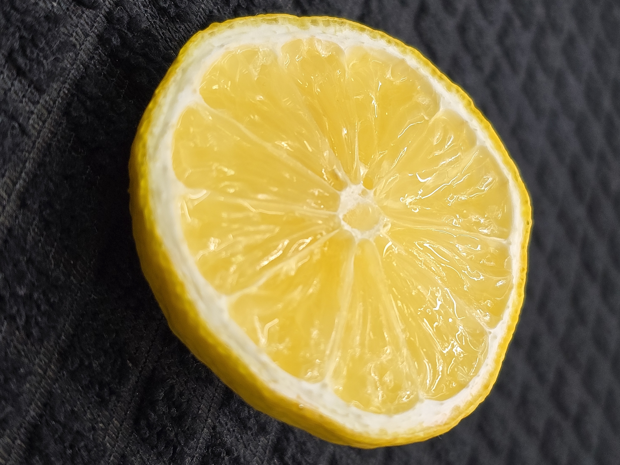 A slice of lemon rests on a dark, textured surface. The lemon slice is bright yellow with visible segments and a white rind. The surface appears to be a dark cloth or fabric with a subtle weave pattern. There are no people or specific locations within Chișinău, Moldova discernible in this image.