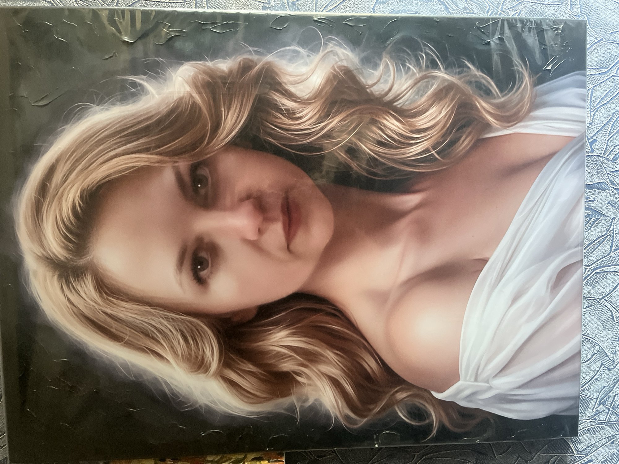 A painting of a woman with blonde hair, wearing a white off-the-shoulder dress, is depicted against a dark background. The woman's hair is styled in loose waves, framing her face. Her eyes are looking directly at the viewer. The dress is made of a sheer fabric, with gathered details around the neckline and sleeves. The painting has a realistic style, with soft lighting and subtle shading. The location is not specified in the image itself.