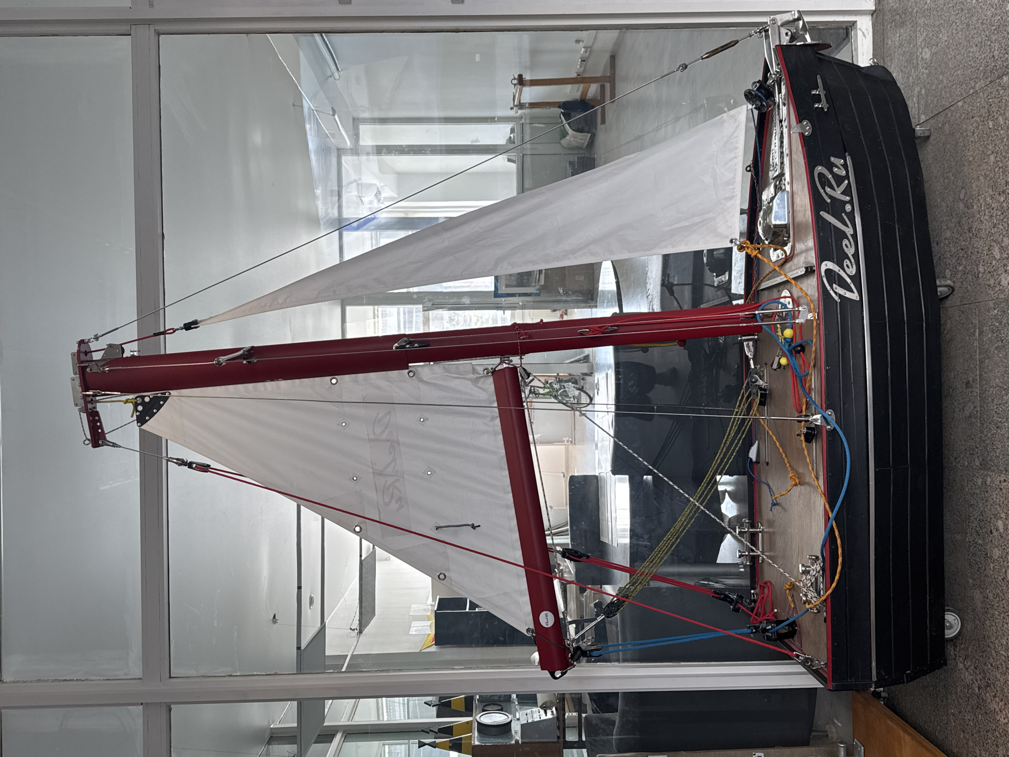 A detailed model sailboat with white sails and red and black trim is displayed in what appears to be a glass case within a modern building. The name "Deal.Ru" is written on the boat's side. The environment reflects a contemporary architectural style with large windows. While the image provides detailed insight into the model boat and its display, the specific location within Saint Petersburg, Russia cannot be determined from the visual information provided. The focus is solely on the object and its immediate surroundings.