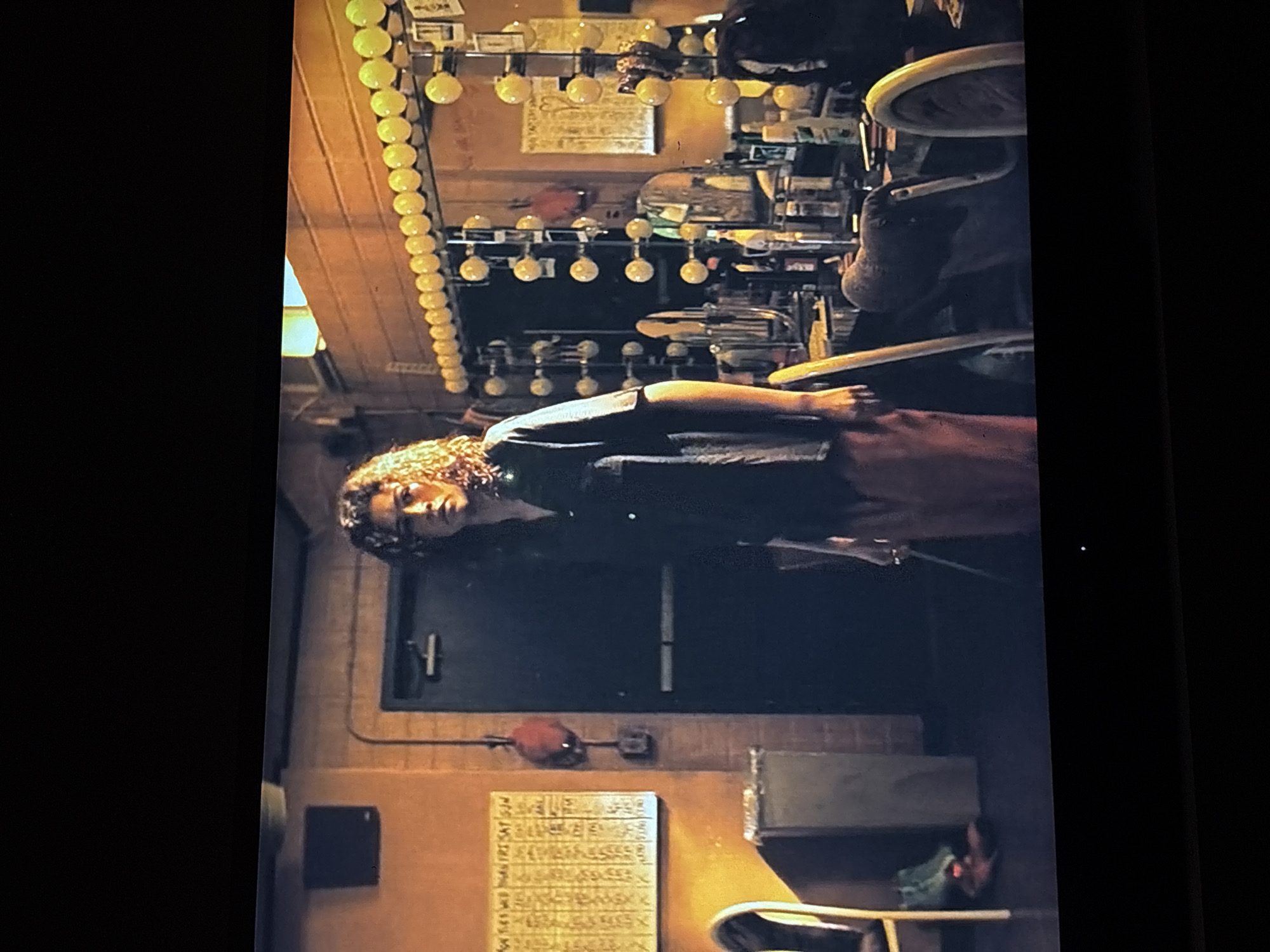 The image appears to show a person with curly hair standing inside a building. Behind them is a door, an electrical box and a poster on the wall. Above them are some stage lights. Without more specific details, I can't confidently identify the exact location as Mexico City or provide more precise details about the scene.
