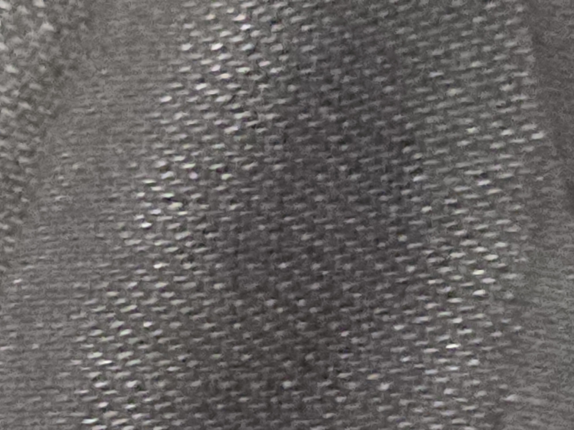 The image shows a close-up, abstract view of a textured gray fabric. The fabric appears to have a woven pattern with small, lighter-colored fibers interspersed, creating a speckled or speckled effect. The texture is consistent throughout the frame, with no discernible objects or discernible elements of a cityscape. The lighting is even, and the focus is on the fabric's surface detail.