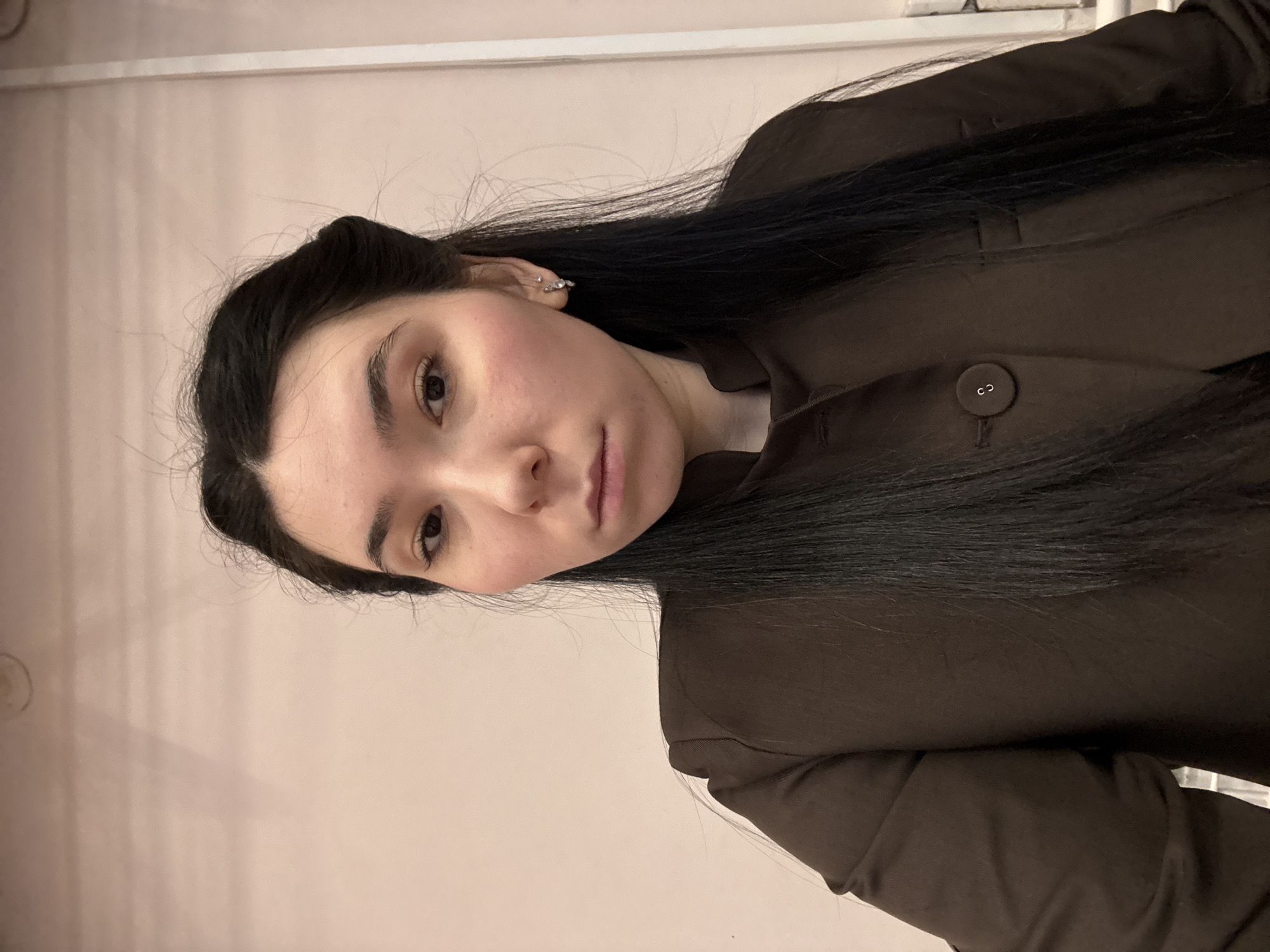 A portrait of a woman with dark hair, wearing a brown blazer against a pale pink background. The location is not discernible as Izhevsk, Russia based on the image.