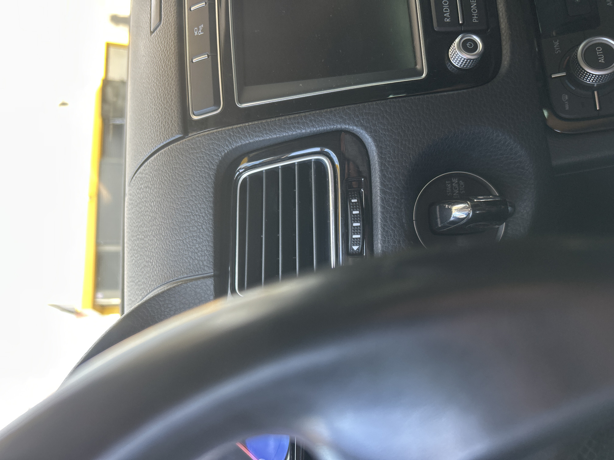 The image shows the interior of a car, likely a Volkswagen Touareg, with a focus on the dashboard. A portion of the steering wheel is visible on the left. The dashboard features a central air vent with chrome trim, a start/stop engine button, a touchscreen infotainment system, and various control buttons and knobs, including those for radio and phone functions, as well as climate control. The interior appears to be in good condition. The exterior environment visible through the windshield suggests a bright, possibly sunny day, with a yellow structure in the background. Based on the context provided, this car is located in Sofiivska Borshchahivka, Ukraine.