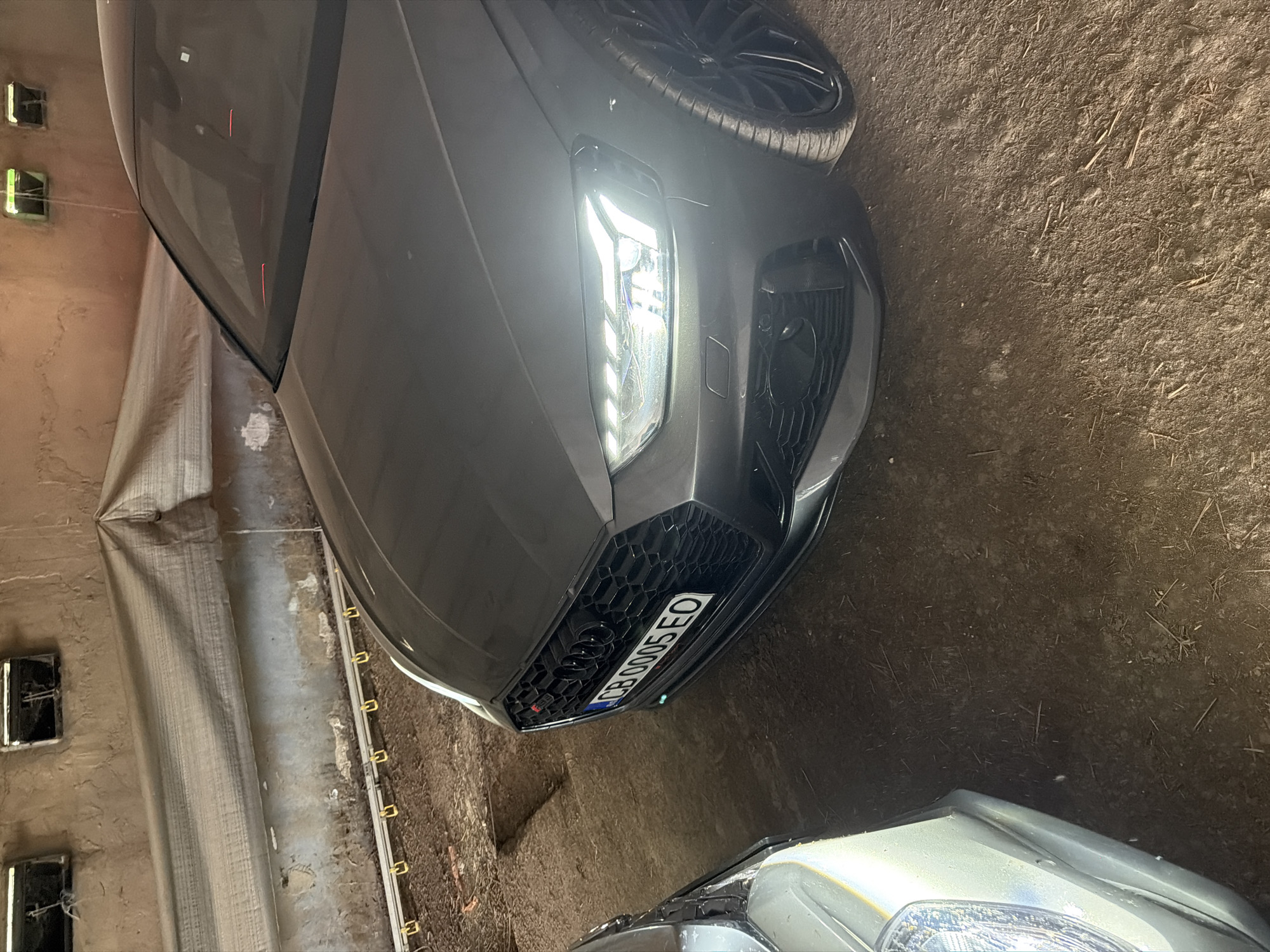 The image depicts the front portion of a grey Audi RS4 parked indoors. The license plate reads "CB 0005 EO," a Bulgarian registration. The surrounding environment appears to be a garage or storage space, with a partially visible second vehicle at the bottom of the frame. The image includes details of a light-colored textured wall on the left side. While the license plate indicates Bulgarian origin, no specific markers in the image directly indicate the location as Chervena voda.