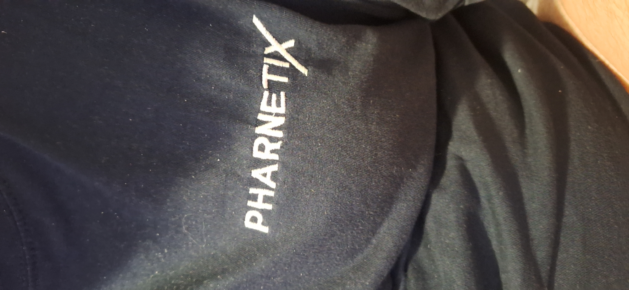 The image shows a close-up of a dark-colored garment, likely a shirt or jacket, with the word "PHARNETIX" printed vertically in white. The location of the image is unknown and cannot be determined from the visual information. There are no people, specific subjects, interactions, or environmental details visible. The background is blurred.