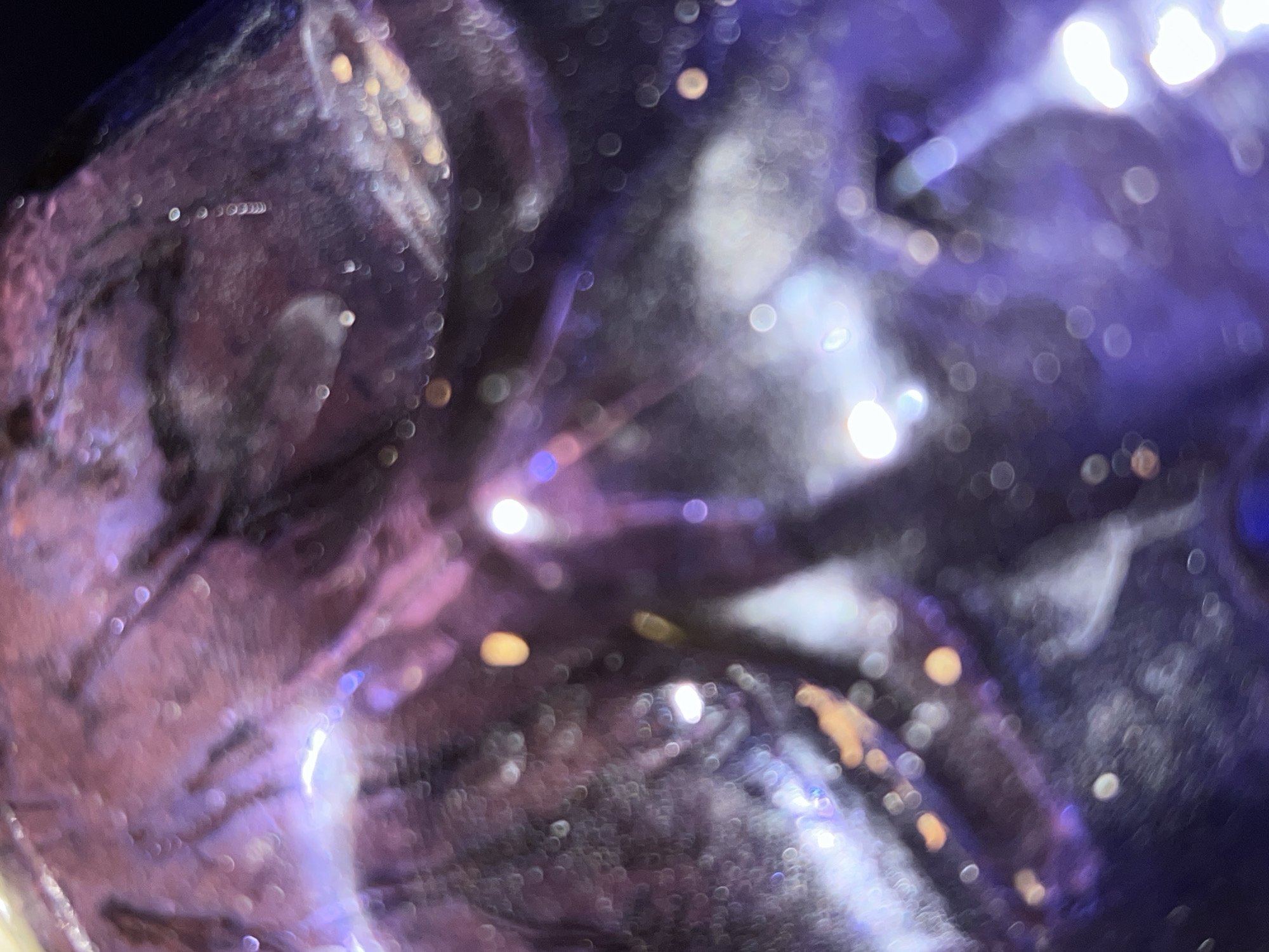 This image is an abstract composition characterized by blurred light and color, rendering specific subjects, objects, or a clear scene unrecognizable. Dominant hues are deep purples and blues, interspersed with bright white and warm orange-yellow highlights. The entire frame is significantly out of focus, creating numerous circular bokeh effects that suggest light sources or reflections viewed through a shallow depth of field or a translucent, textured material.
Fluid, indistinct shapes and wavy patterns are formed by the interplay of light and shadow, evoking the impression of light refracting or reflecting off a crinkled or irregular surface. Intense points of white light are scattered throughout, particularly prominent as bright streaks and concentrated glows in the upper right and central areas, contrasting sharply with the darker, cooler tones.
No people, discernible objects, or specific environmental features are visible within the image. Consequently, no activity or event is depicted. The abstract nature of the photo prevents any determination of the time of day, weather conditions, or specific location cues from the visual content alone. No text is visible. The overall impression is one of ethereal light play and soft luminescence. The provided location, Picassent, Spain, is external context not visually present in the image.