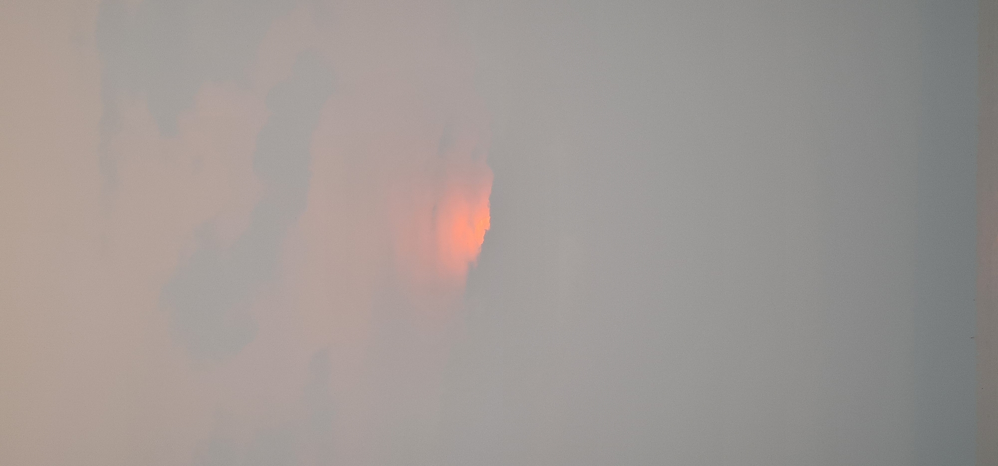 The image shows a sky obscured by heavy fog or smog, with a small, orange-colored sun barely visible through the dense atmosphere. The setting is likely urban, but the lack of visibility prevents any specific identification. There is no information regarding any specific location within Đà Nẵng, Vietnam. There are no people, subjects, objects, or actions immediately discernible in the image due to the heavy obscuration.