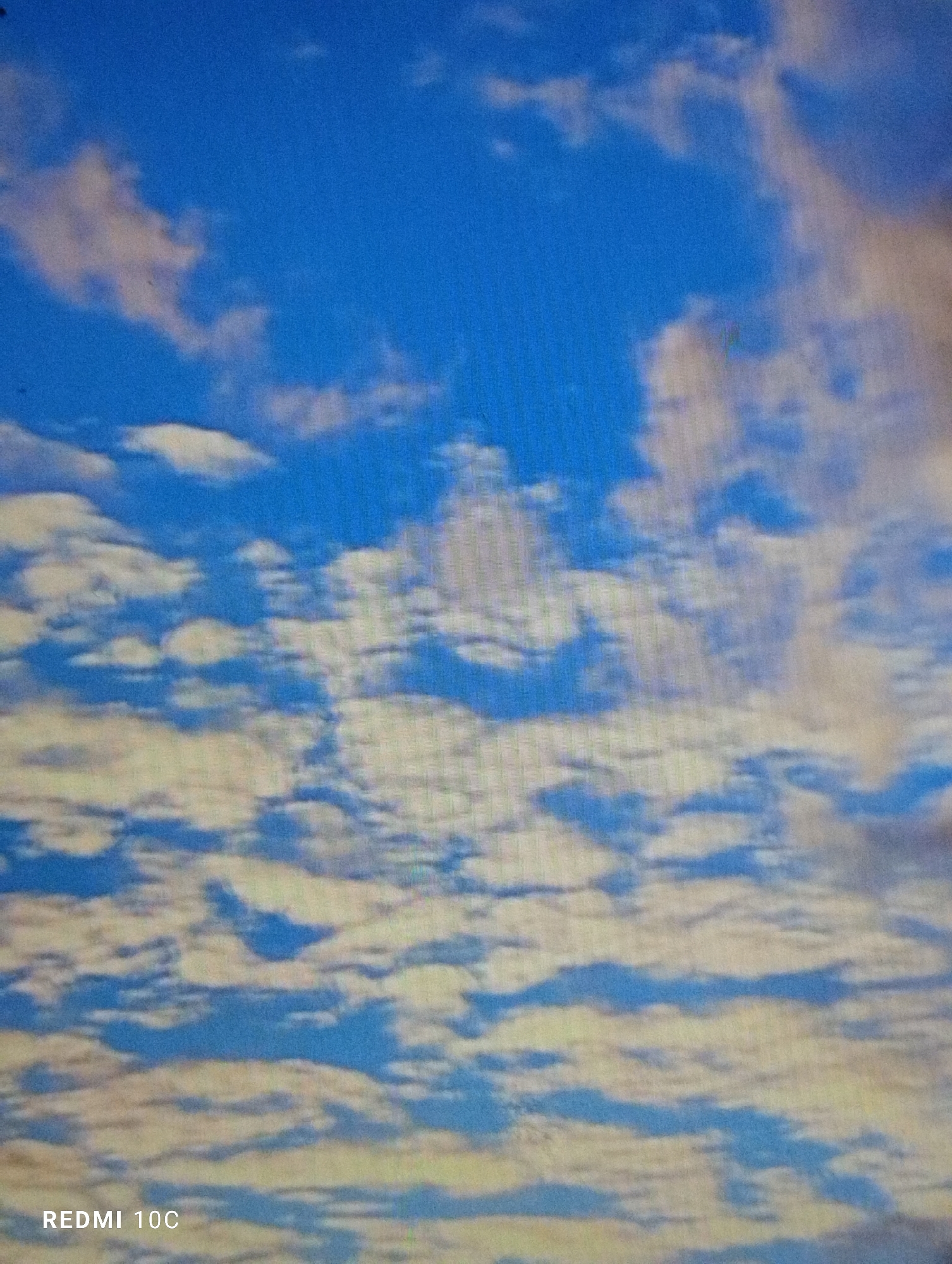 The image shows a daytime sky with blue patches and many small, white altocumulus clouds. The photo was taken with a Redmi 10C. The location is Tinaquillo, Venezuela.