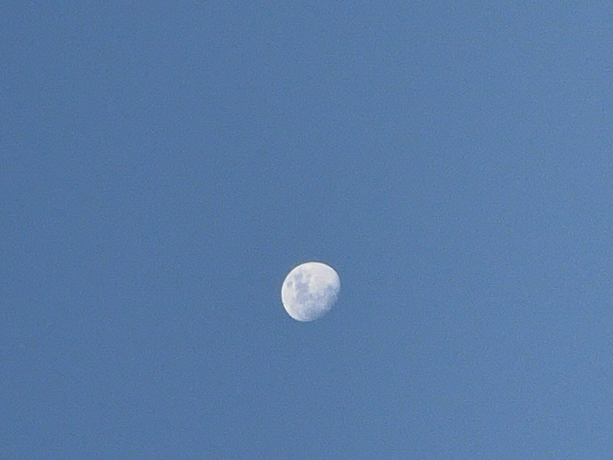 The image shows a crescent moon in a clear blue sky. The location is not discernible from the image.