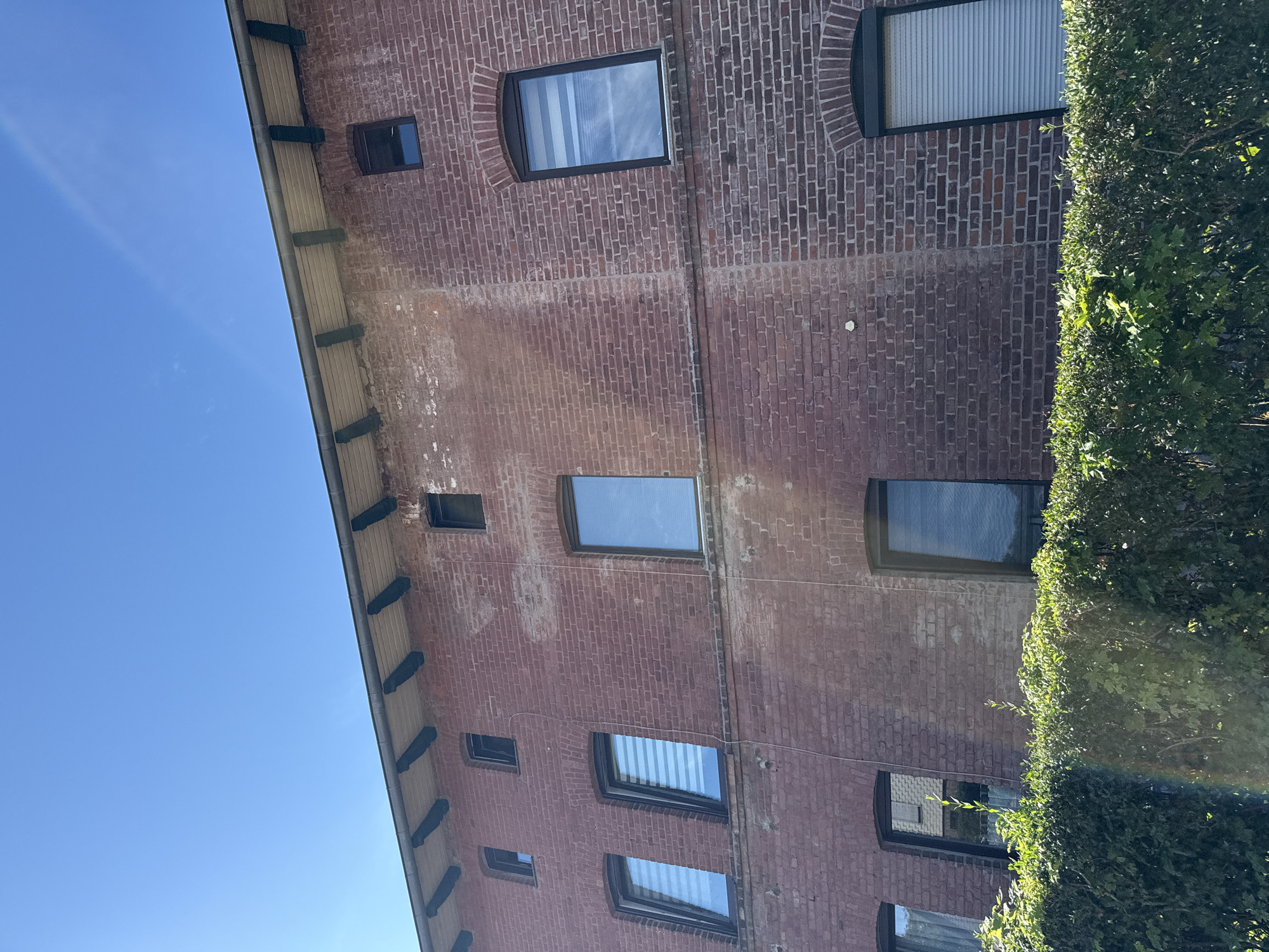 A brick building with several windows and a red tile roof is shown under a clear blue sky. The building is located in Walkenried, Germany. A hedge is visible in front of the building.