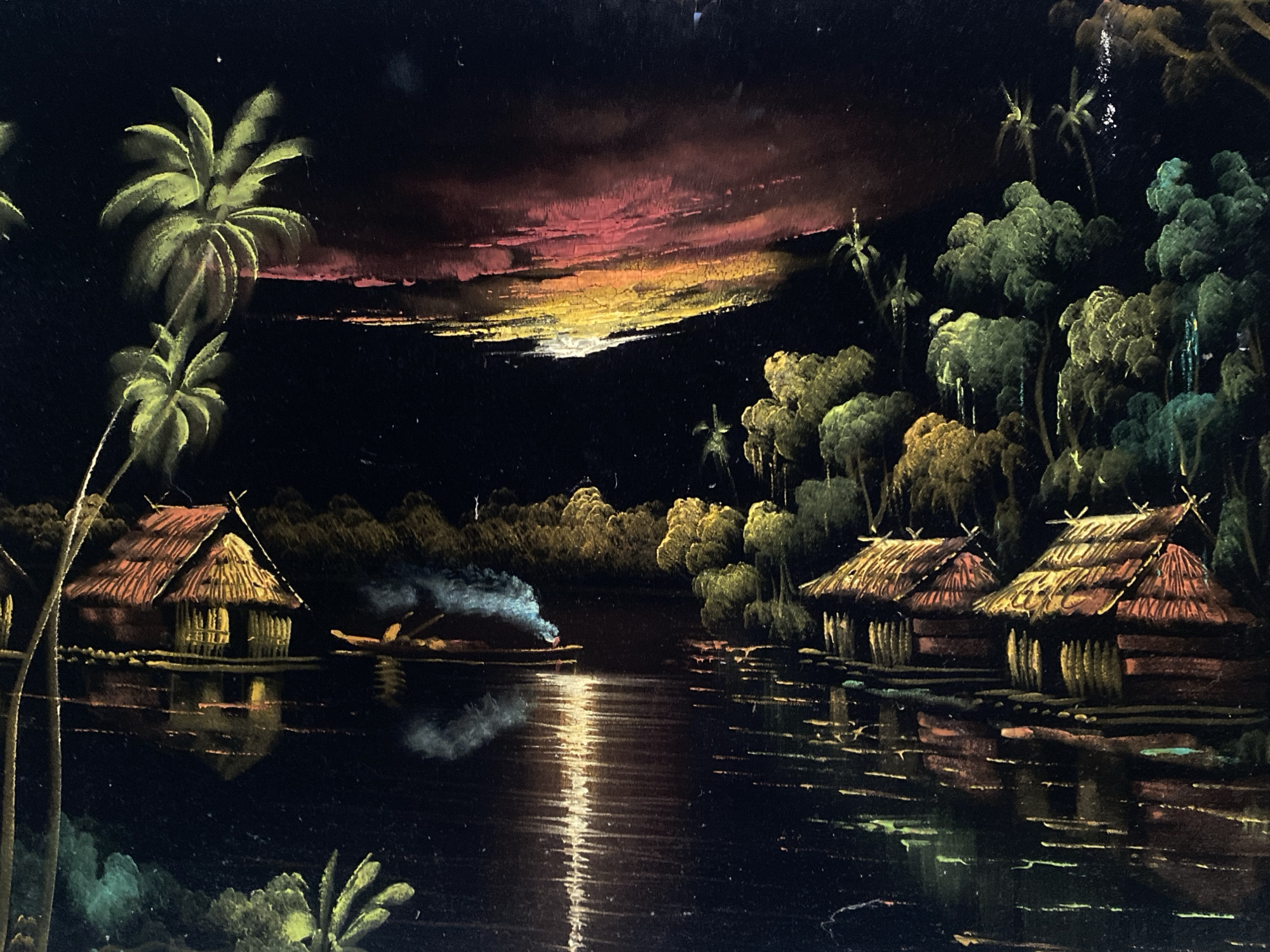 This painting depicts a vibrant, nocturnal river scene in a tropical setting, possibly characteristic of regions like Tinaquillo, Venezuela. The dark canvas is brought to life by glowing colors, creating a dramatic atmosphere of twilight, likely dusk or dawn.
The scene features a tranquil river reflecting various light sources. On the left bank, two prominent palm trees with luminous green fronds stand tall, partially obscuring a traditional thatched hut built on stilts over the water. Its warm interior glow is subtly reflected below. In the middle distance, a small boat or canoe, possibly with occupants, glides across the water, emitting a plume of white smoke or mist. This boat is positioned within a strong, shimmering vertical reflection of light on the water's surface.
The horizon is ablaze with a spectacular array of reds, oranges, and yellows against a dark sky, indicative of a vivid sunset or sunrise. The riverbanks are densely forested with lush green foliage and additional palm trees. On the right side, a small cluster of similarly constructed thatched huts with warm, inviting glows are situated by the water's edge, their shapes and colors partially mirrored in the dark river.
The overall impression is one of peaceful, remote village life amidst abundant tropical nature. No visible text is present in the image.