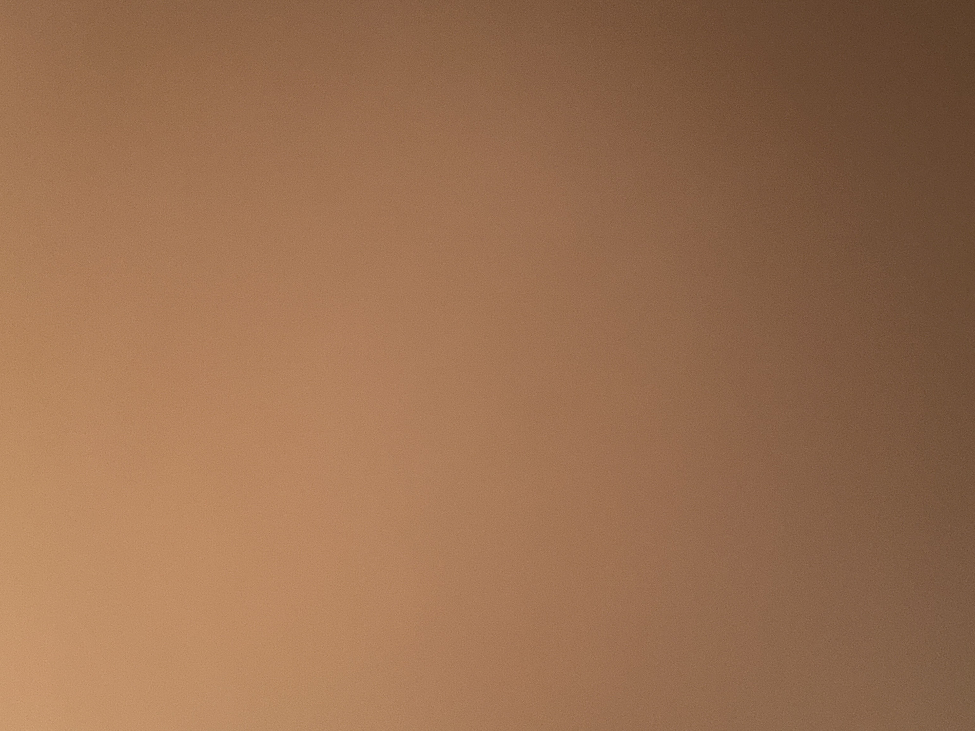 The image is a close-up, out-of-focus shot of a textured, uniform surface. The color is a warm, light brown, resembling brushed or matte metal, or possibly a textured fabric. There are no discernable objects, people, or environmental features. The image is devoid of any details that would suggest a specific location within Tay Nha Trang Ward, Vietnam, or any other place. The grainy texture is consistent across the entire frame.