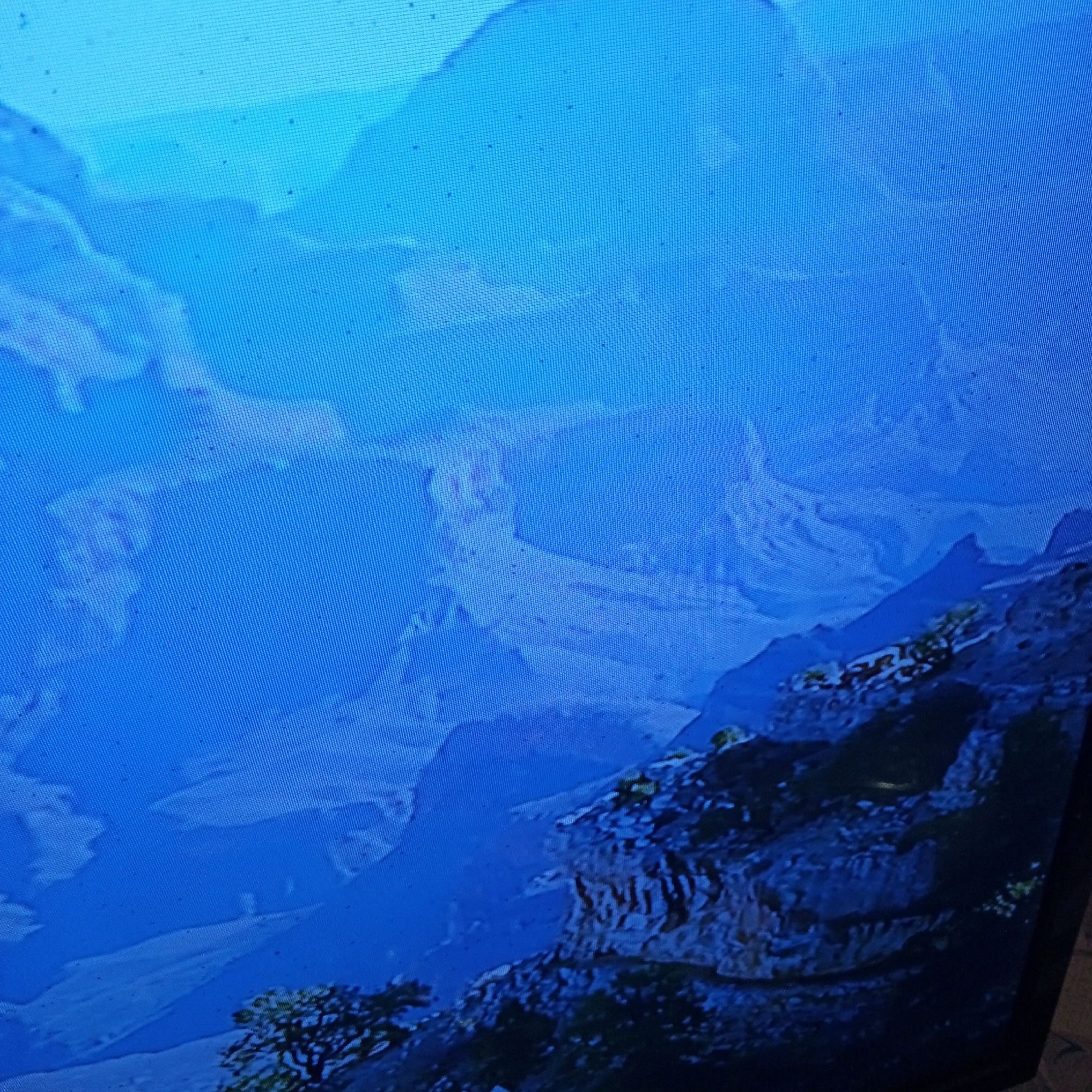 The image depicts a vast, blue mountainous landscape, possibly a digital rendering or a photograph of a screen displaying such an image, given the visible pixelation and grid pattern. The scene is dominated by shades of blue, suggesting a cool atmosphere or perhaps twilight.
In the foreground, a rocky, textured cliff face is visible, with patches of green, possibly vegetation or moss, clinging to its surface. A dark, silhouetted tree with intricate branches is positioned to the left, partially obscuring the view of the distant mountains.
The middle ground and background are filled with layered mountain ranges, fading into a hazy, ethereal blue. These mountains have a sculpted, almost abstract appearance, with soft edges and flowing forms. Some appear to be snow-capped or covered in mist, further contributing to the atmospheric depth. The overall impression is one of immense scale and natural grandeur, with a serene and slightly melancholic mood.
There are no visible people or specific objects that would indicate a particular activity or event. The time of day is ambiguous, but the deep blues and soft lighting suggest either early morning, late evening, or a digitally created environment. The weather appears to be calm, with no indication of storms or wind. The location is unknown, but the mountainous terrain evokes a sense of wilderness and isolation. There is no visible text in the image.