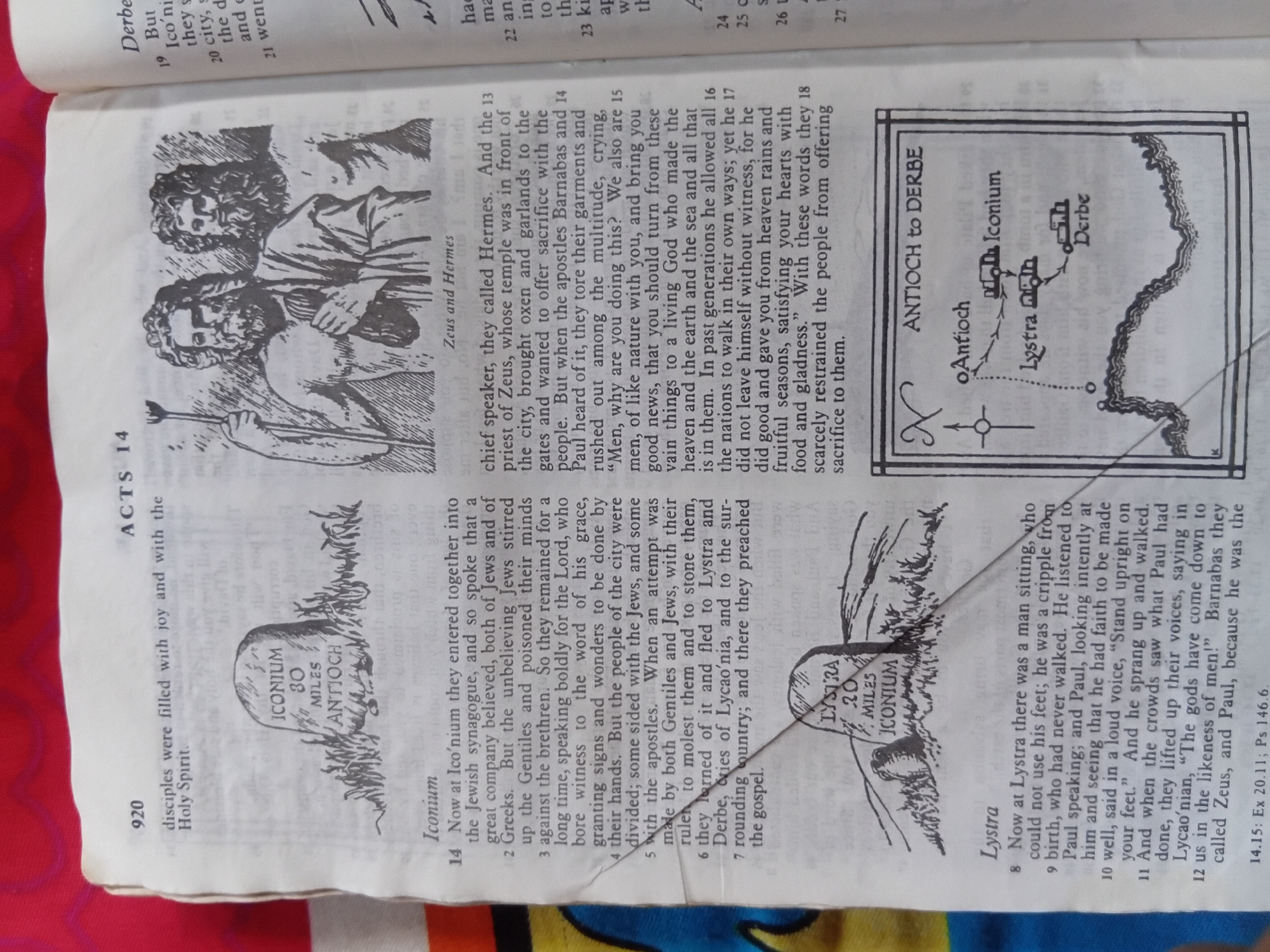 This media file is a photograph of an open book, likely a Bible, showing text and illustrations related to biblical events. The image is shot at an angle, with the book resting on a red surface.
The left page features an illustration of two figures, identified by text as "Zeus and Hermes." Below this illustration is a section of text with the heading "ACTS 14" and the verse number "920". The text describes disciples filled with joy and the Holy Spirit, and the events in Iconium.
The right page displays text detailing events in Iconium and Lystra, including attempts to worship Barnabas and Paul as gods. There are also two illustrations on this page: a map showing a route from Antioch to Derbe, passing through Iconium and Lystra, and a drawing of a stone marker or monument with text "LYSTRA 20 MILES ICONIUM". The text on this page mentions chief speaker, Hermes, priests of Zeus, and apostles Barnabas and Paul. It also describes a man at Lystra who was healed by Paul and the subsequent reaction of the crowd who believed the gods had come down to them in human form.
Visible text includes chapter and verse references, names of biblical figures and places like "ACTS 14", "Zeus", "Hermes", "Barnabas", "Paul", "Iconium", "Lystra", "Derbe", and "Antioch". There are also biblical citations such as "14.15: Ex 20.11; Ps 146.6". The overall scene depicts religious narrative through text and visual aids within the pages of a book. The setting appears to be an indoor environment, given the lighting and the presentation of the book.