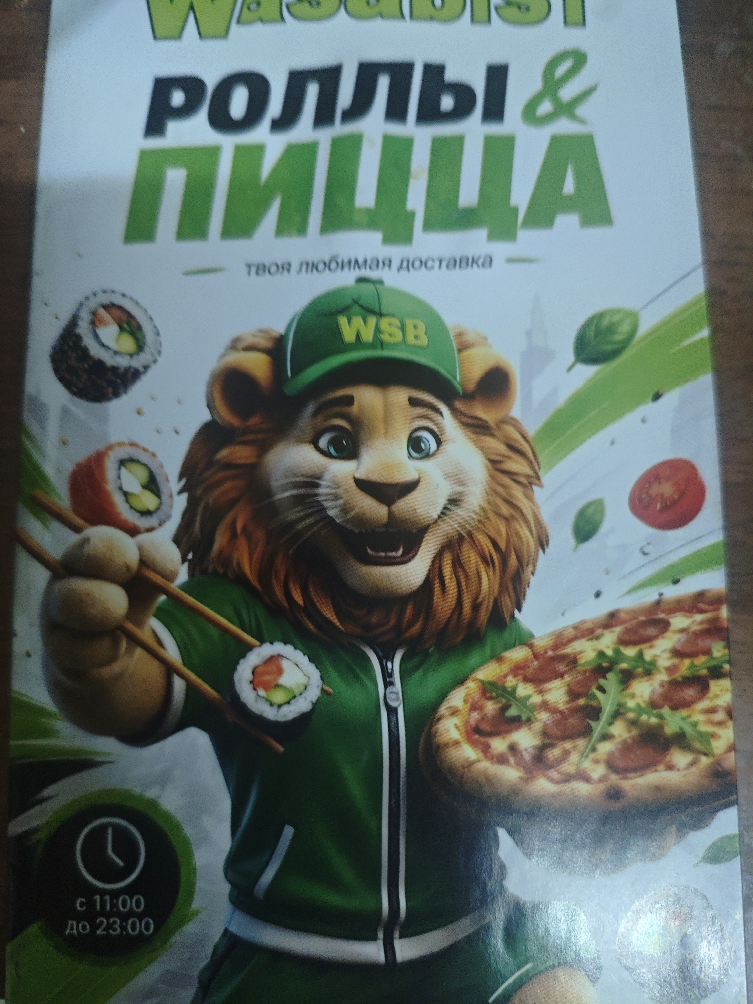 The image is a promotional poster for a food delivery service called "WASABI" which offers "ROLLS & PIZZA". The central subject is a cartoon lion wearing a green baseball cap with "WSB" on it, a green jacket, and holding chopsticks with sushi. In the background, there are images of sushi rolls, a pizza, tomatoes, and basil leaves. At the bottom left of the poster, there is a clock icon with the text "с 11:00 до 23:00", indicating operating hours from 11:00 to 23:00. The poster does not contain any information about the city of Armavir, Russia.