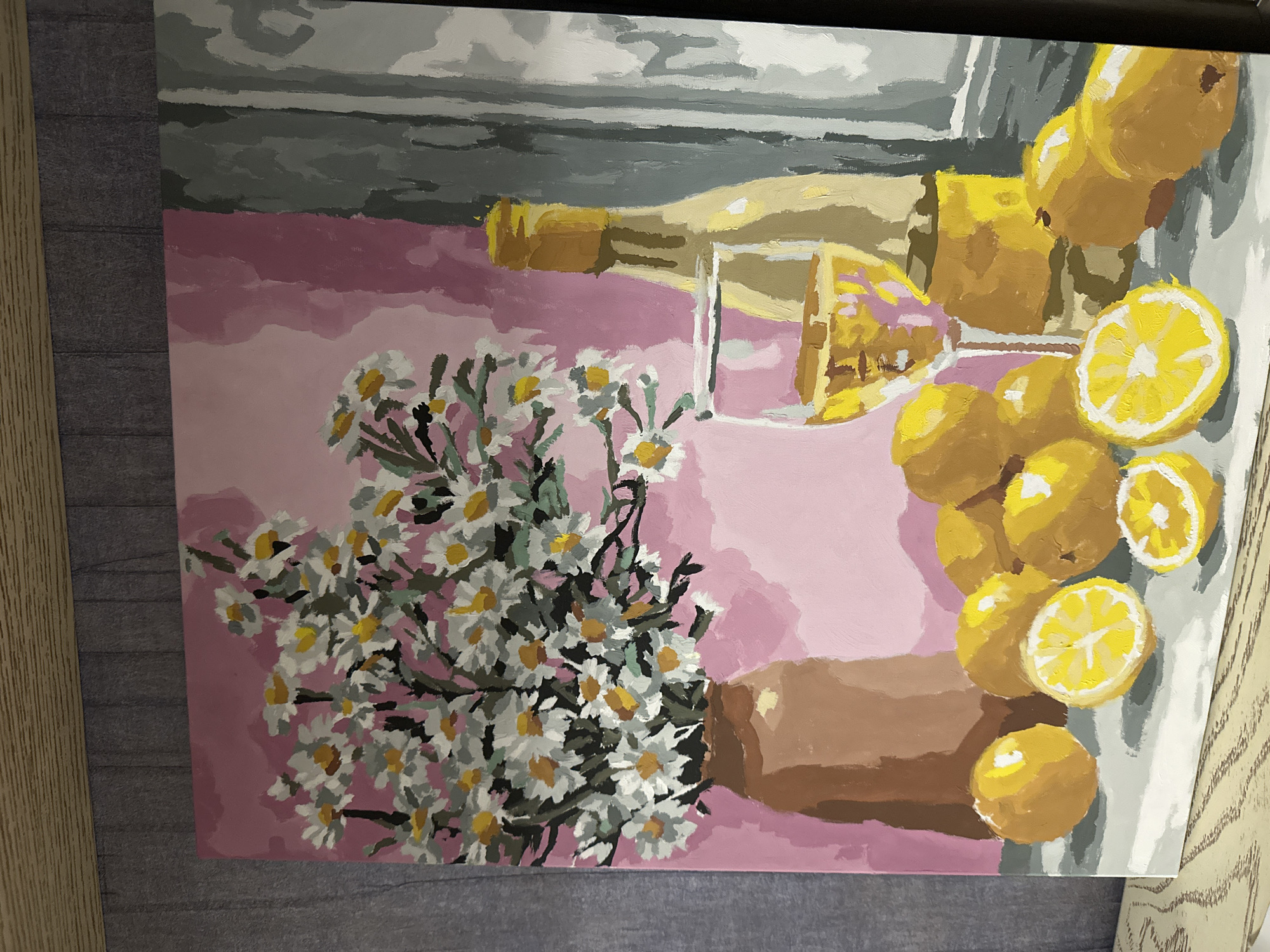 The image is a still-life painting. A vase of white and yellow flowers sits on a pink surface to the left. To the right, a wine bottle and a glass are laid down. A pile of lemons are stacked on the right of the canvas. The background is gray. It is unclear if the scene is in Yerevan, Armenia.