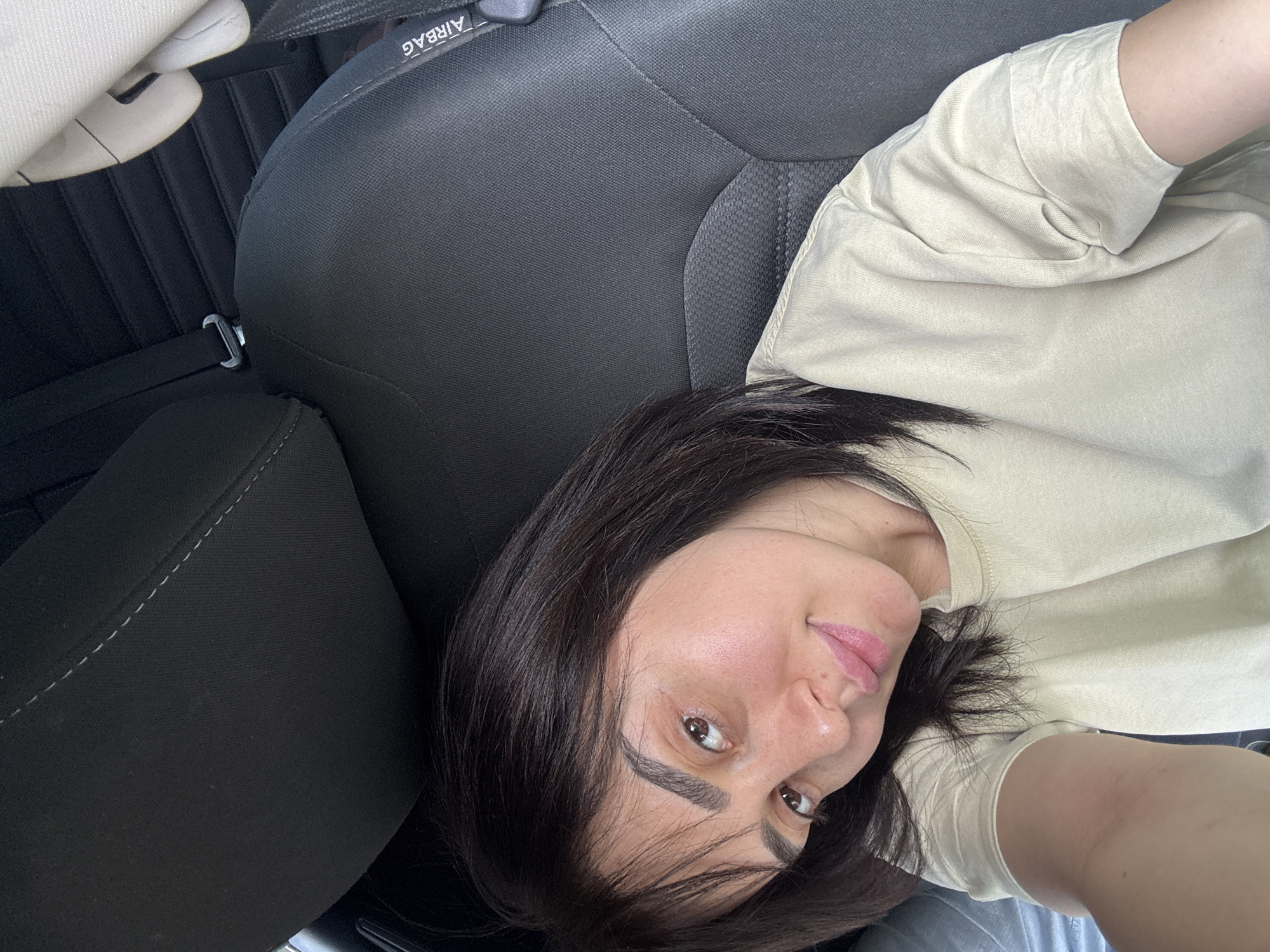 A woman with dark hair is visible, seated in what appears to be the driver's seat of a car. The car seat is upholstered in a dark fabric. The headrest features an 'AIRBAG' label. The specific location within Tbilisi, Georgia, cannot be determined from the available visual data.