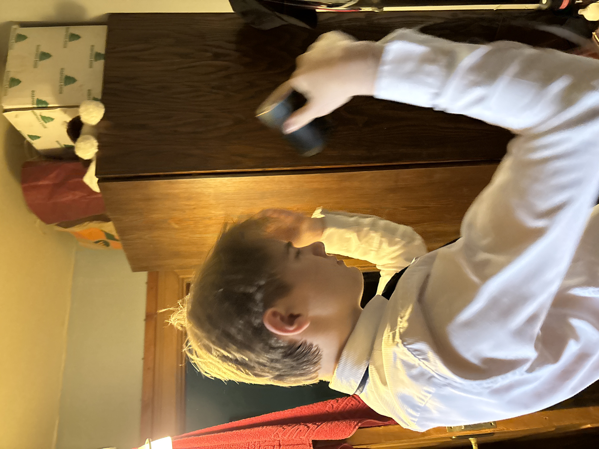 A person in a white collared shirt is holding a black object. A box and a dresser are nearby. The location is an indoor scene in an Unknown city.
