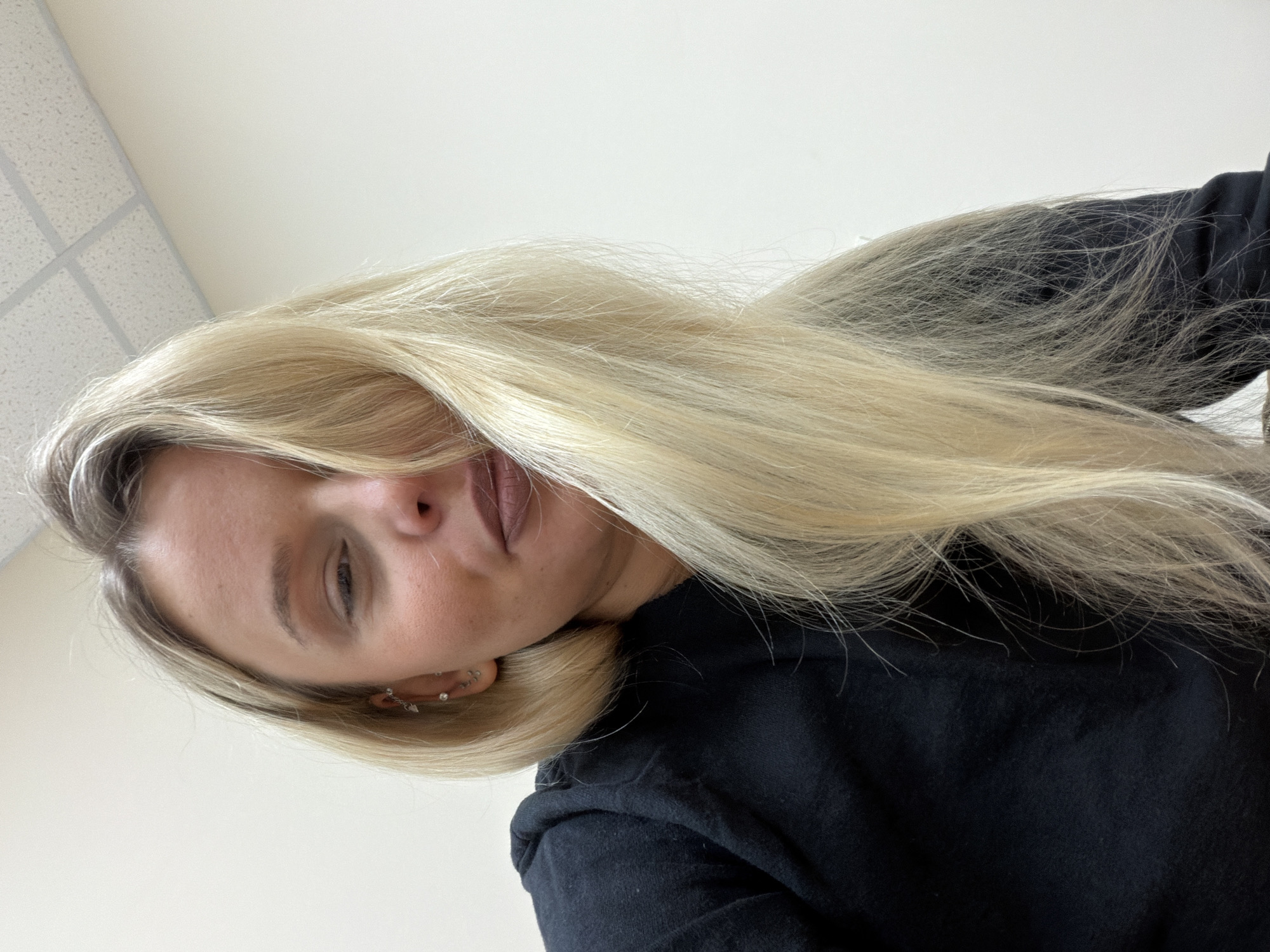 A woman with long blonde hair is wearing a black top. She appears to be indoors, with a white ceiling with a grid pattern visible in the background. The image appears to be taken at an angle, possibly as a selfie. No elements indicate the location of Sarapul, Russia.