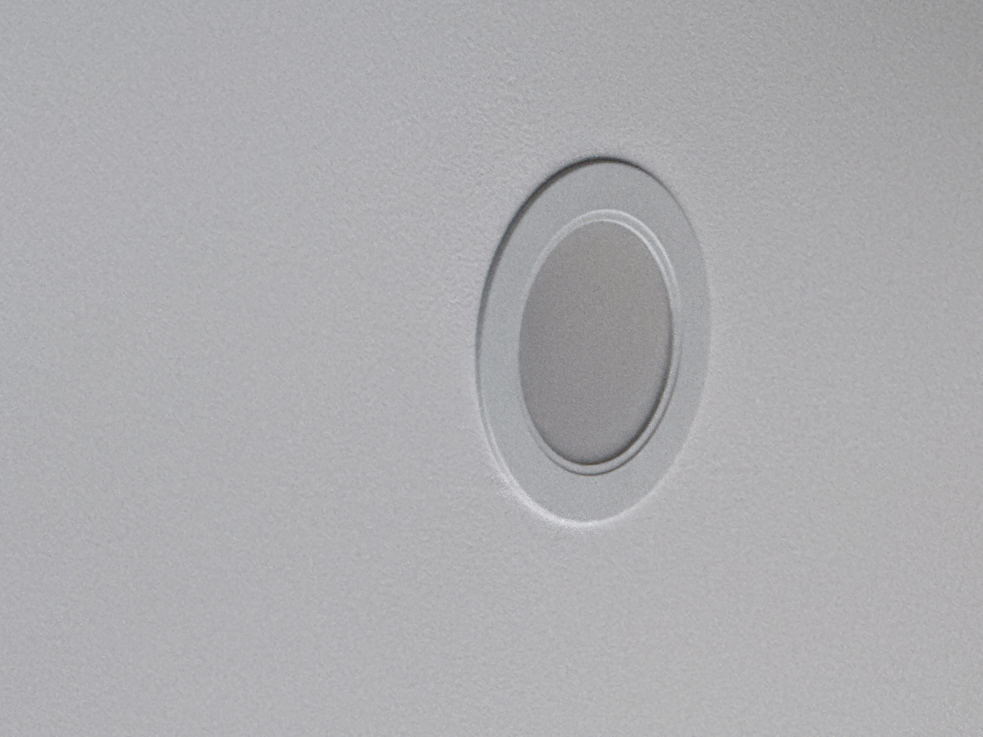 The image shows a close-up of a recessed ceiling light fixture. The fixture is circular with a matte gray finish. It's comprised of a recessed central disc surrounded by two concentric rings. The ceiling surface around the fixture is a textured, flat white. The environment is devoid of people and any other objects apart from the ceiling and light fixture. The location in the city of Lovech, Bulgaria, cannot be determined from the image.