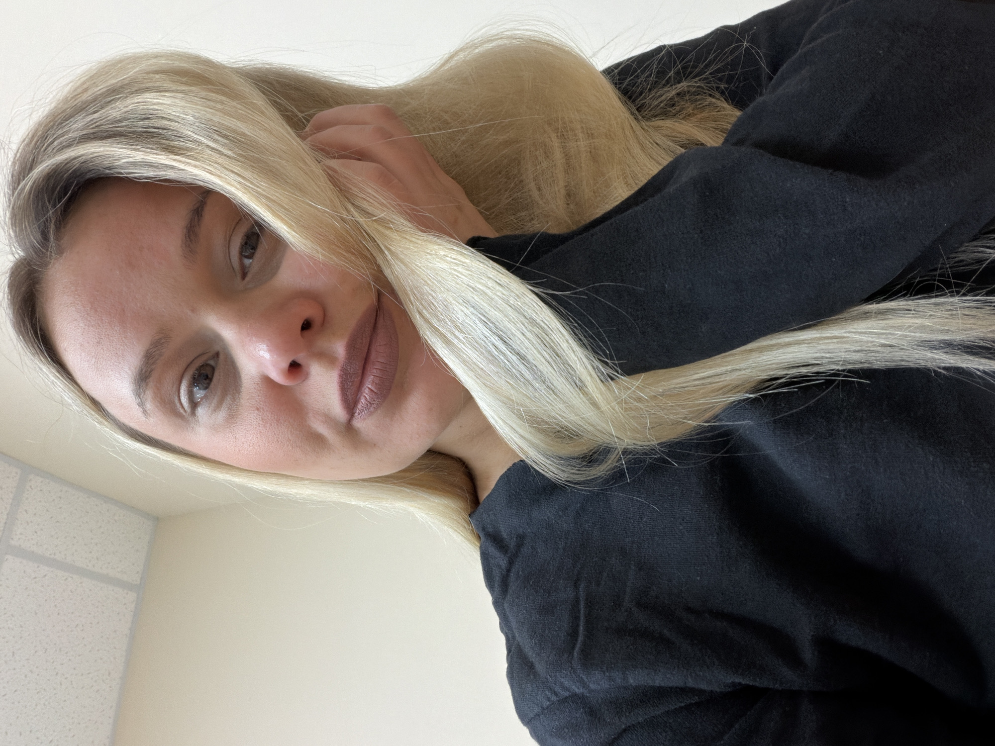 A woman with blonde hair, wearing a black long-sleeve shirt, is looking down at the camera. The background appears to be an interior space with a beige wall and a ceiling with textured tiles. The location is not discernible based solely on the image. The city of Sarapul, Russia cannot be confirmed from this image alone.