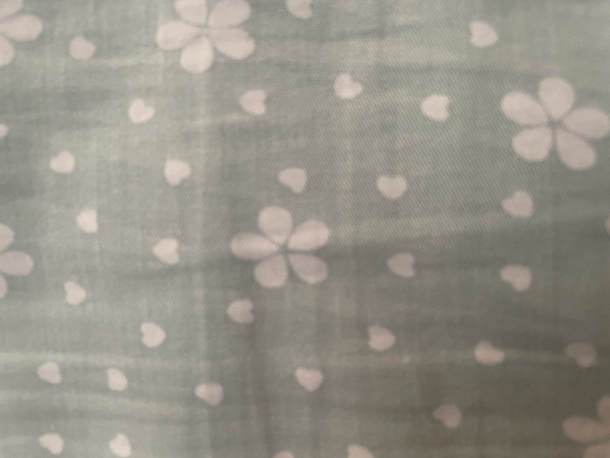 The image displays a light blue fabric with a repeating pattern of small white hearts and five-petaled flowers. The pattern is evenly distributed across the fabric. The image does not depict any recognizable landmarks or features that would allow for its location to be identified within the city of Tashkent, Uzbekistan. There are no people, actions, or interactions visible in the image.