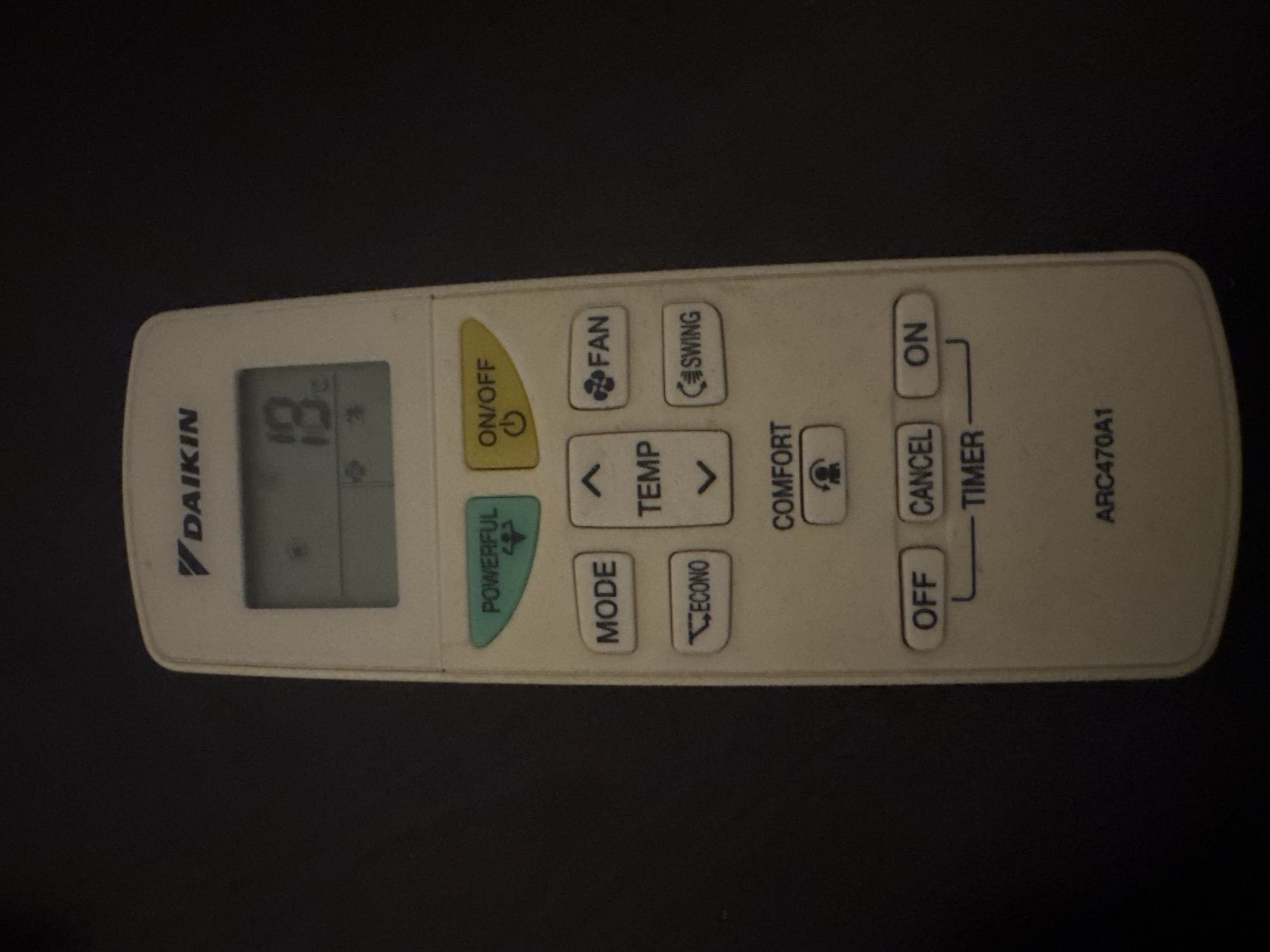 The image shows a Daikin air conditioner remote control lying on a dark, seemingly flat surface. The remote is white and has a display showing "18°C". The buttons are labeled with functions like "ON/OFF", "FAN", "SWING", "TEMP", "MODE", "ECONO", "COMFORT", "OFF", "CANCEL", "ON", and "TIMER". The model number "ARC470A1" is printed on the right side. There is no indication of the location of Sarnevo, Bulgaria, or any other information about the environment or people.