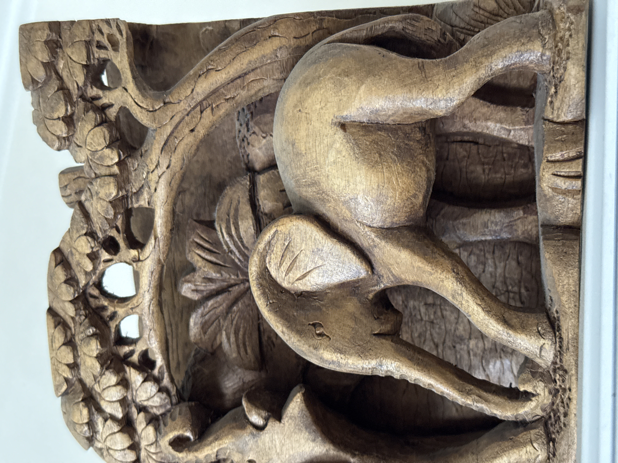 The image depicts a detailed wood carving featuring an animal, potentially an elephant, surrounded by ornate floral and leaf designs. The carving appears to be part of a larger architectural element, possibly a corbel or bracket. The wood has a warm, golden brown tone with visible grain. Specific details suggest the animal is a elephant due to the presence of a trunk, legs, and what could be interpreted as ear. The overall style suggests a historical or traditional artistic influence. The location of the carving is listed as Unknown, Russia.