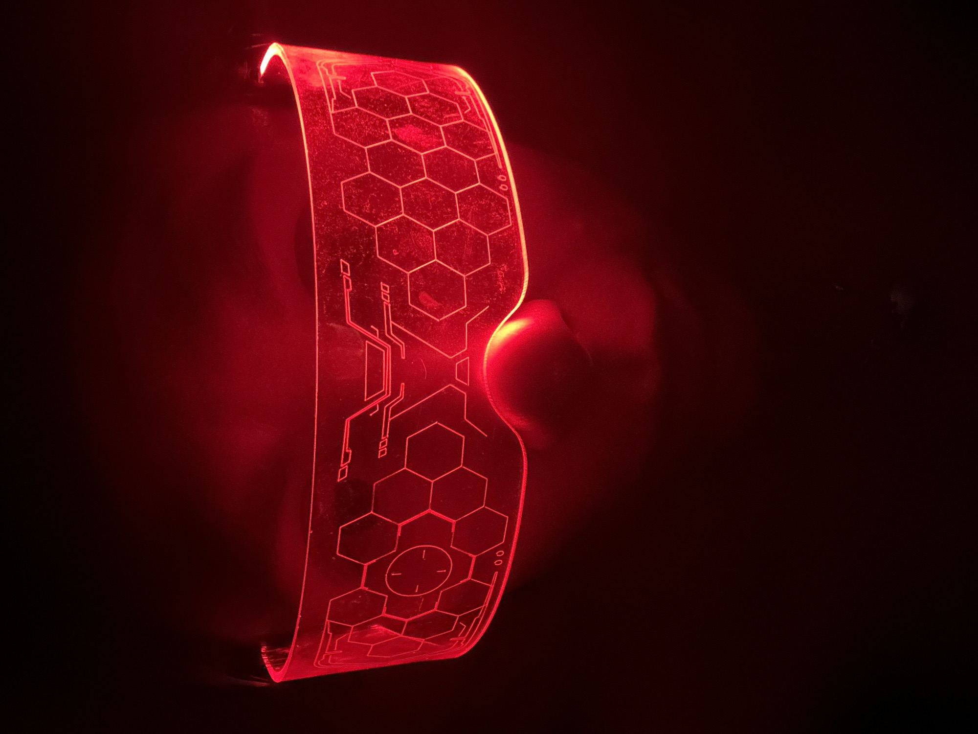 A photograph depicts a pair of futuristic-looking glasses illuminated with red light. The glasses feature a geometric design with a prominent hexagon pattern and circuit-like graphics. The background is dark, creating a dramatic contrast that highlights the glowing eyewear. The location in Votkinsk, Russia, is not determinable from the image.
