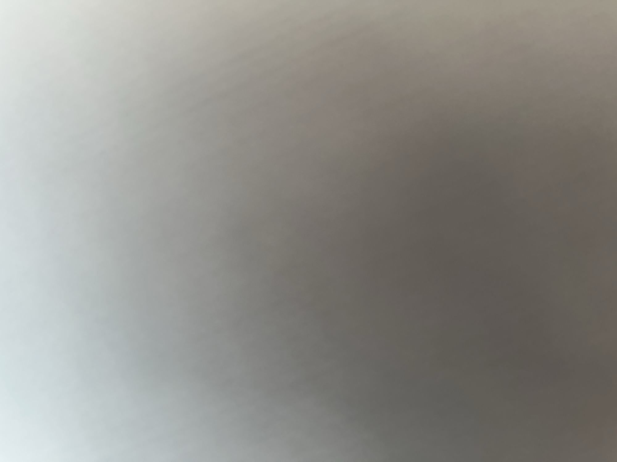 This is an abstract image with no discernible subjects, objects, scene, or activity. The image is an out-of-focus gradient of light gray to a darker gray, suggesting a smooth, featureless surface or a very diffuse light source. There are no visible details such as time of day, weather, location cues, or emotions. There is no visible text.