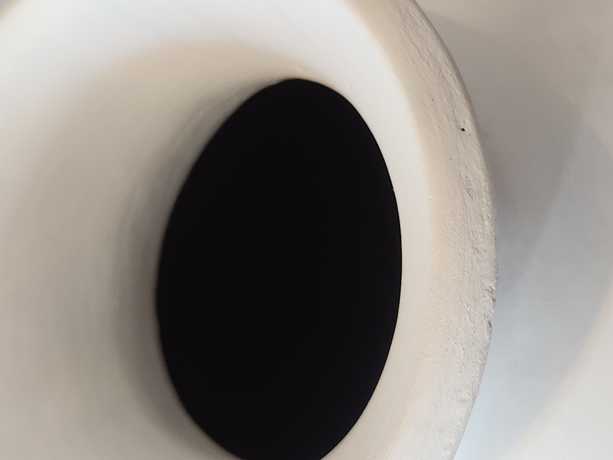 The image shows a close-up view of the interior of a white ceramic vase. The opening of the vase is a wide, dark, circular void, with the white ceramic curving outwards and upwards from its edges. The texture of the ceramic is rough and uneven, with a few small dark specks visible on its surface. The lighting casts a soft shadow on the lower part of the vase. The image does not contain any information about its location in Maitland, United States of America, nor does it depict any people or actions.