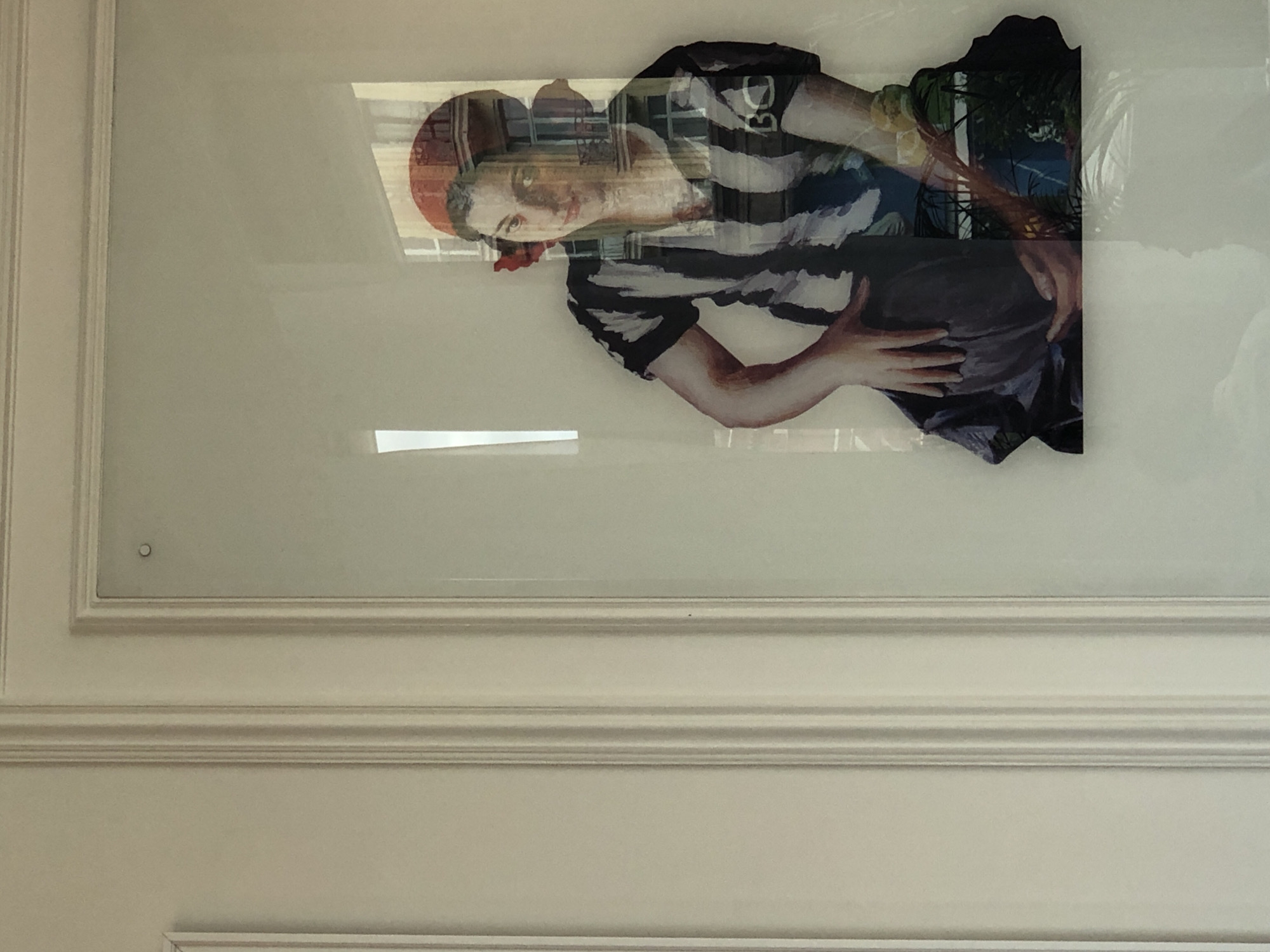 A framed artwork hangs on a white wall. The frame consists of two layers of decorative molding. The artwork is a depiction of a person wearing a striped shirt and a red cap, holding a dark object. The artwork also shows a landscape background. The artwork appears to be hanging in a room with a window, as there is a reflection visible on the artwork. Without additional context, it is impossible to know the exact location in Moscow, Russia.