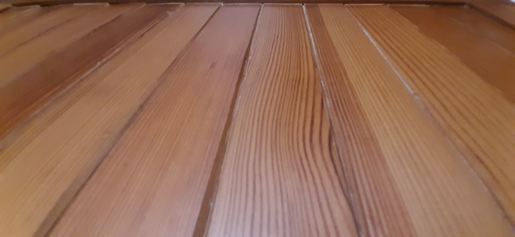 The image shows a close-up, angled view of wooden slats, possibly from a fence or a building exterior. The wood is light brown with visible grain patterns. The slats are horizontal and appear to be mounted close together. There are no people or other objects visible in the frame. The lighting suggests an outdoor environment. The image is too abstract to determine its specific location within Yessentukskaya, Russia.