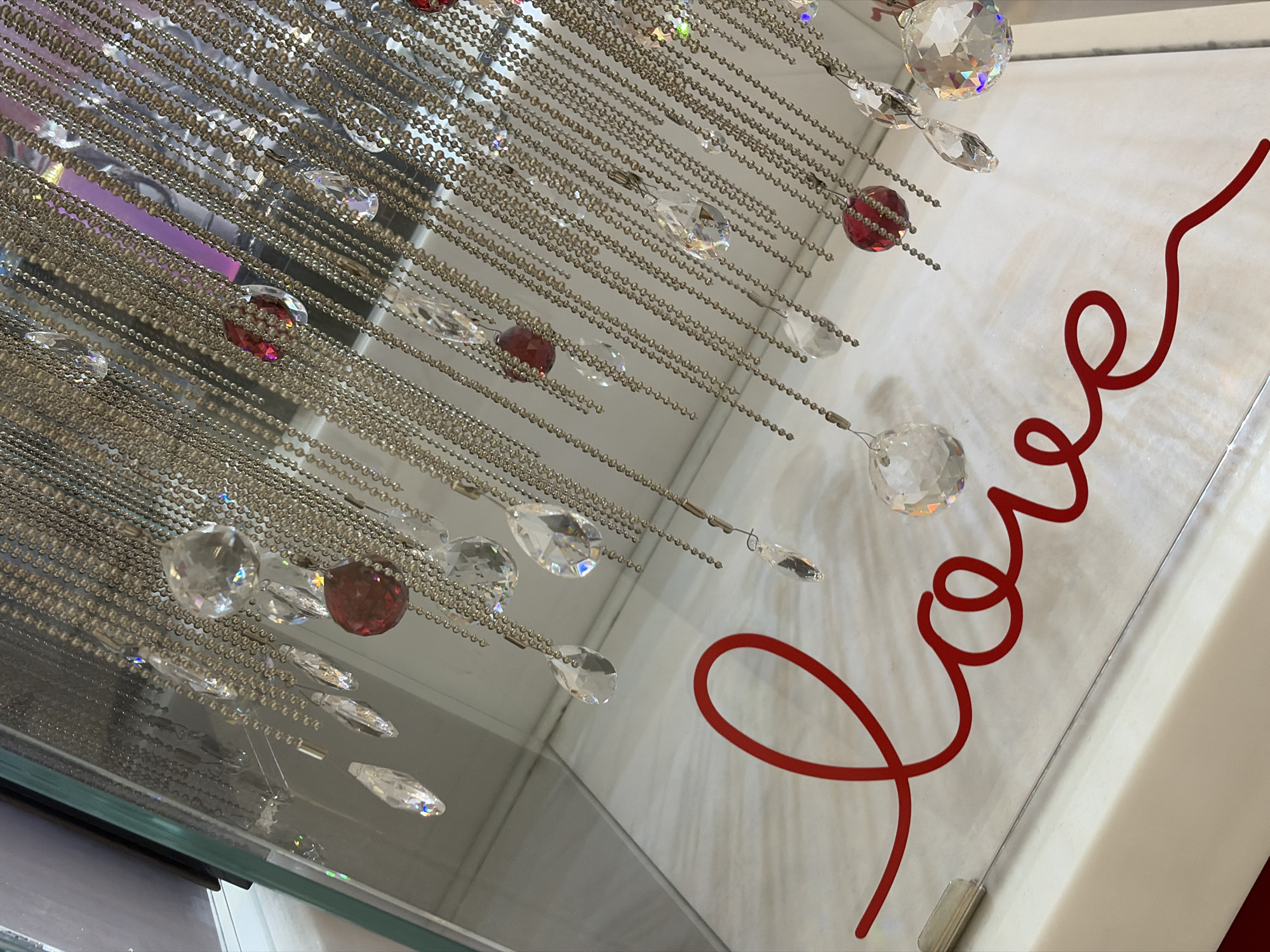 The image features a decorative object against a white background, possibly a wall or surface. The object consists of strands of beads and crystals hanging down, some clear and some red. To the right, the word "love" is written in cursive using a red hue. The overall setting and subject suggest a retail or decorative environment. Specific location in Saint Petersburg, Russia is not discernible from the provided image.