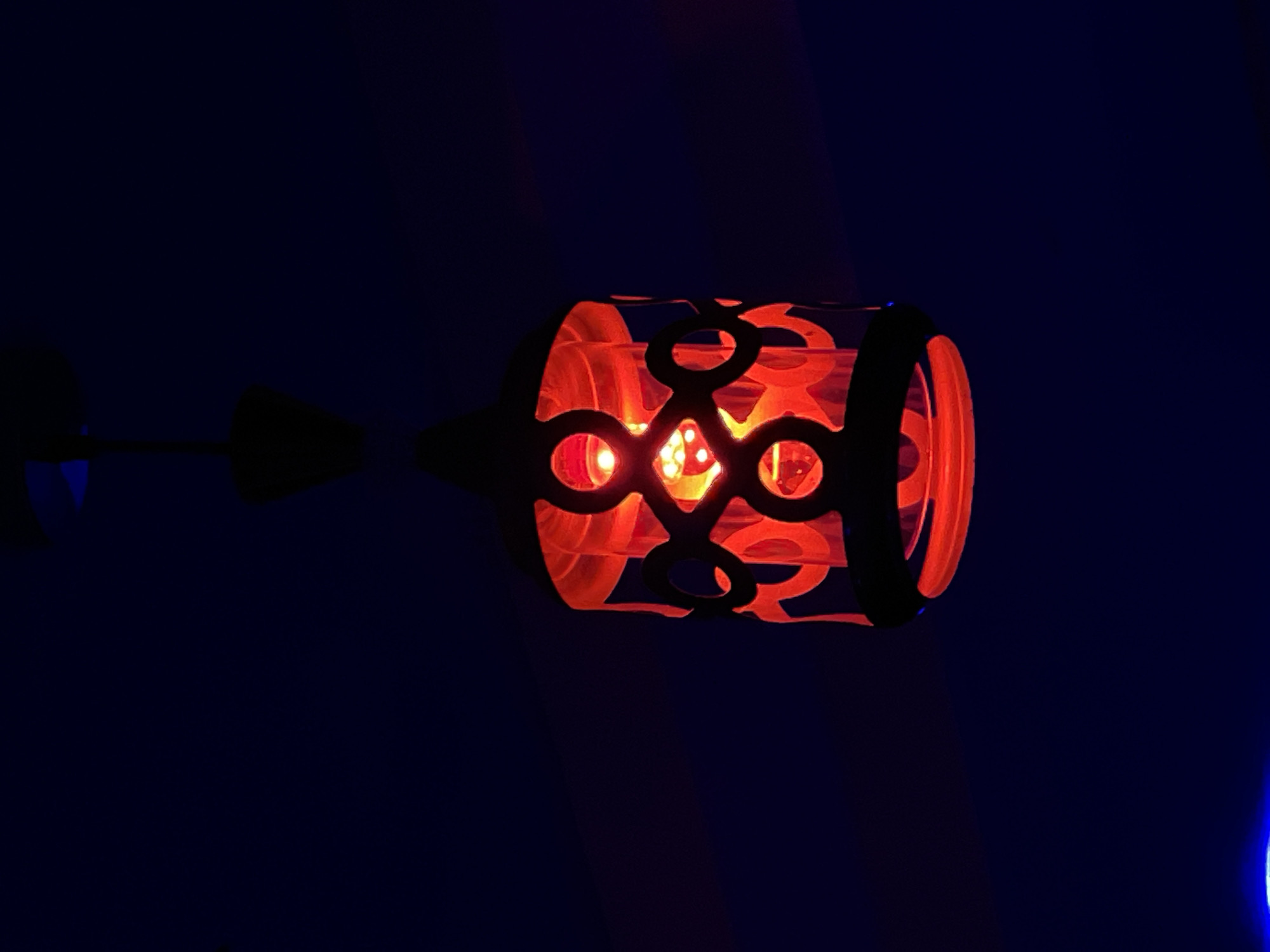 The image shows a red lantern hanging from a ceiling. The lantern has a patterned shade with cutouts that reveal the red light within. The background is dark blue, with a hint of blue light at the bottom of the image. The scene appears to be indoors, in a dimly lit environment. The location of this image in the city of Durimi, Nigeria, is not discernible from the visual information provided. There are no people, actions, or interactions visible in the image.