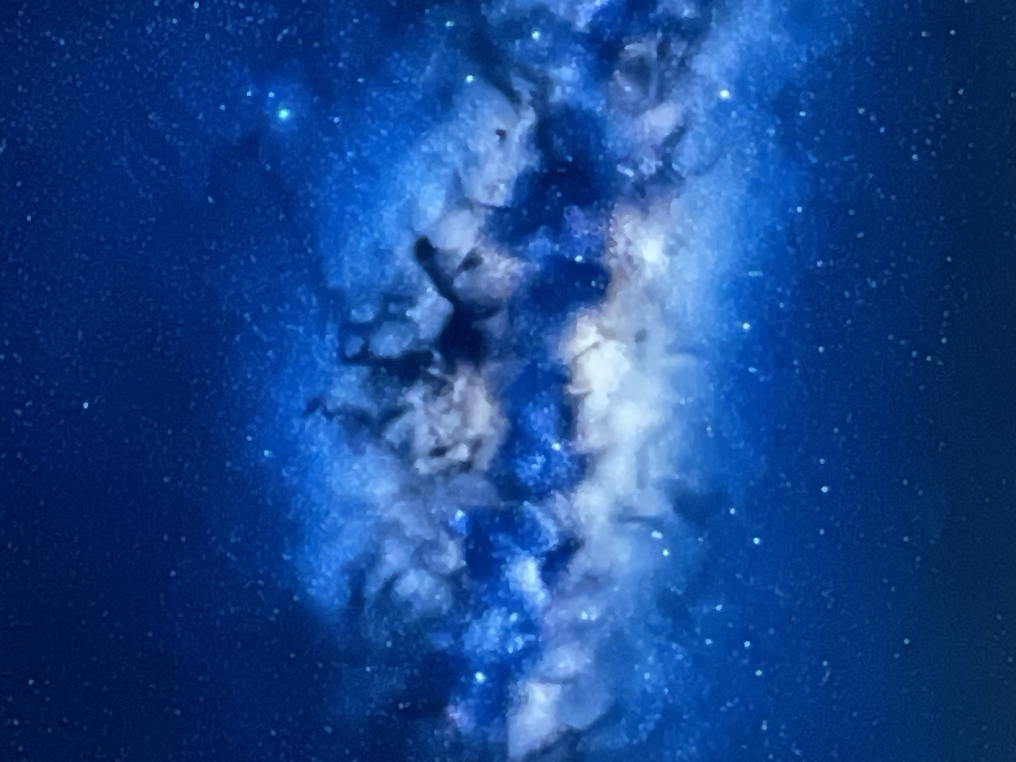 The image is a close-up, abstract depiction of the Milky Way galaxy. It features swirls of bright white and vibrant blue cosmic dust and gas, interspersed with darker, shadowy regions. Numerous small, white specks represent distant stars. The overall impression is one of immense depth and cosmic beauty. There is no discernible location in the city of Denpasar, Indonesia, or any human presence depicted in this astronomical image.