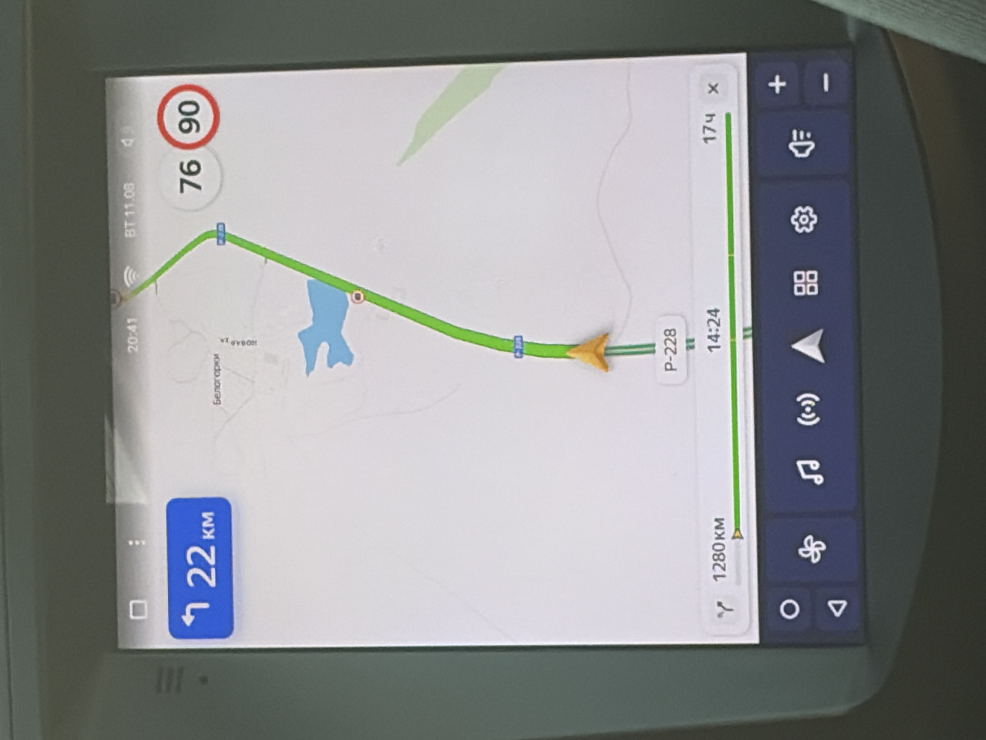 The image shows a GPS navigation screen, likely in a vehicle. The map displays a route through a body of water and a road labeled "P-228" in the city of Belogorki, Russia. The current speed is indicated as 76 km/h, with a speed limit of 90 km/h. The remaining distance to the destination is 22 km, and the total distance to the destination is 1280 km. The time is 14:24. Below the map are navigation icons, including a compass, a fan, music, and volume controls.