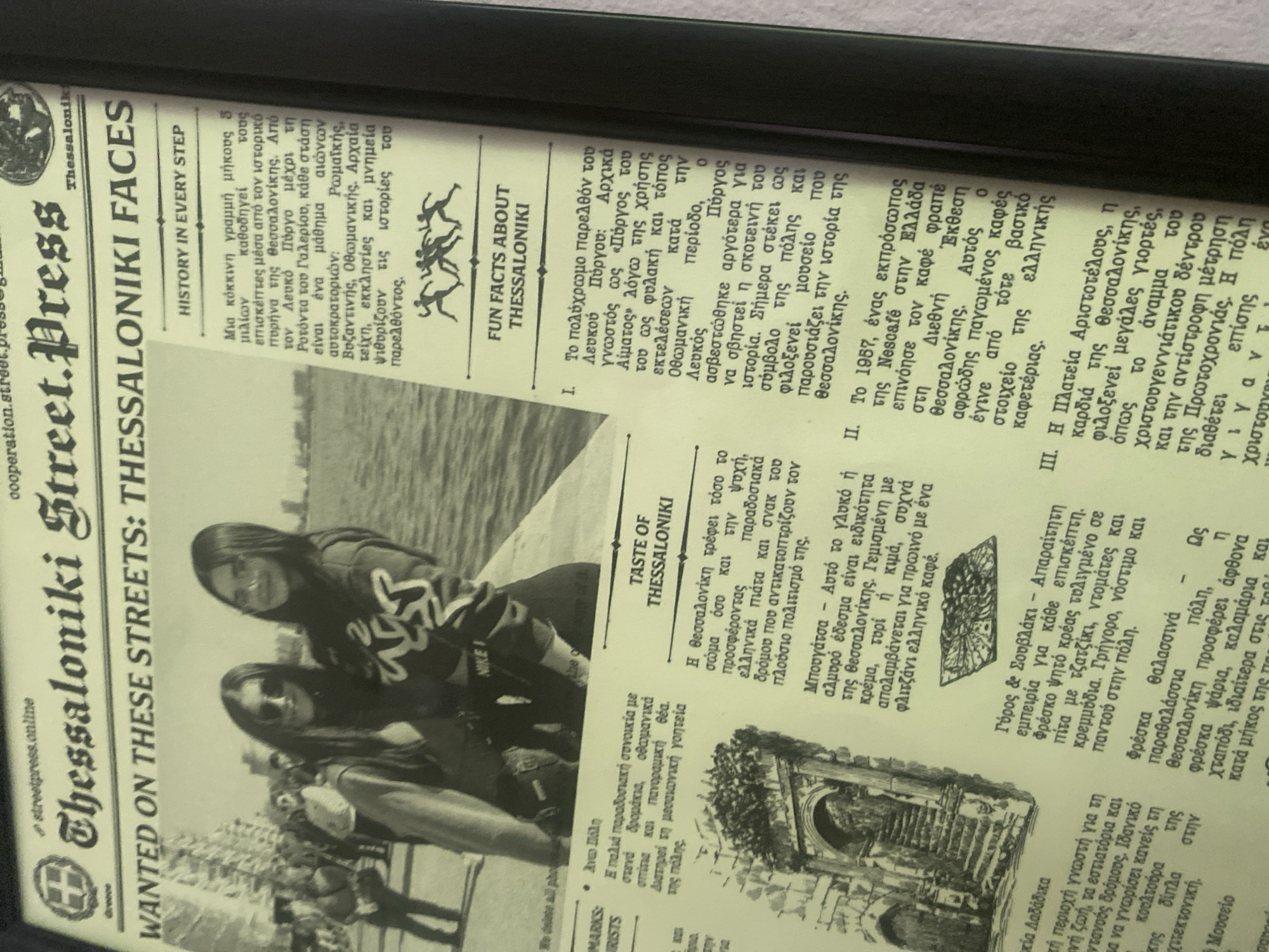 The image shows a framed newspaper article titled "Thessaloniki Street. Press. Wanted on these streets: Thessaloniki Faces." The article includes a black and white photo of two women, presumably the Thessaloniki faces mentioned in the title. The article has several sections with headlines such as "History in Every Step," "Fun Facts About Thessaloniki," and "Taste of Thessaloniki." It is a collection of facts and information about the city of Thessaloniki, Greece. There is no indication of Ivaylovgrad, Bulgaria in the image.
