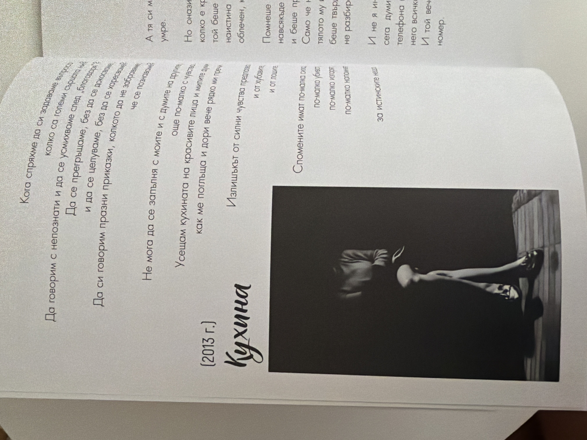 The image shows an open book with text and an illustration. On the left page, below a title that appears to be "Кухня" (Kitchen) and a date "(2013 г.)", there is a black and white photograph of a person, likely a woman, sitting with crossed legs. The person is wearing a sweater and shoes. The background is dark and the lighting is dramatic, focusing on the figure. The right page of the book contains a significant amount of text, presented in paragraphs and shorter lines. The text is in Bulgarian. No location in Pazardzhik, Bulgaria is depicted or mentioned in the image.