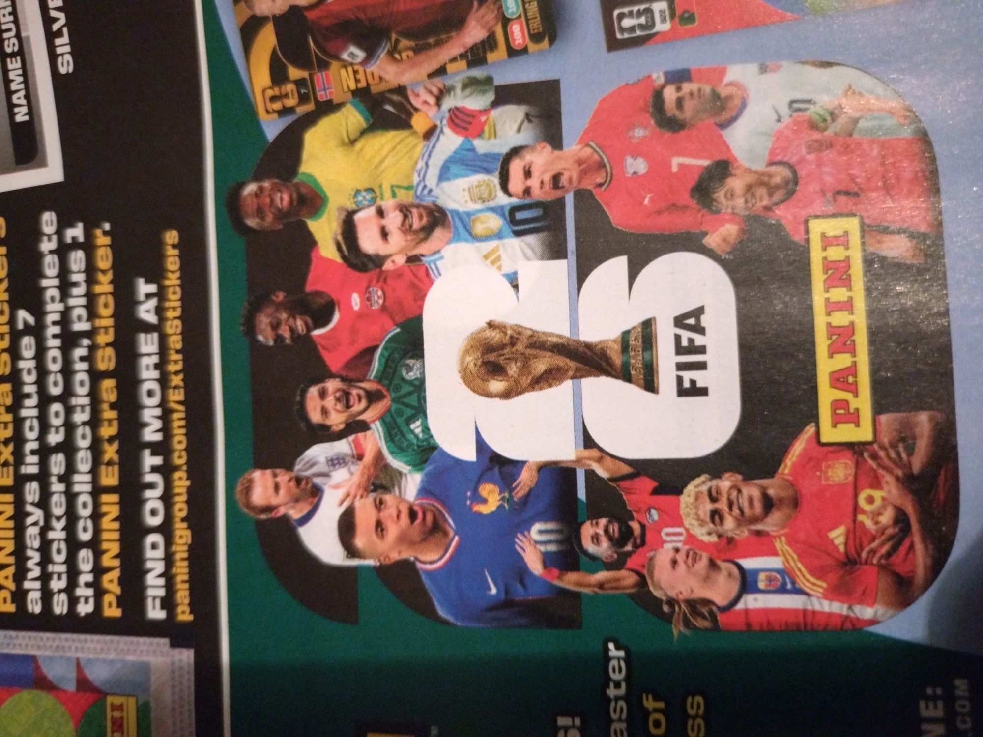 The image shows a promotional display for Panini FIFA World Cup Qatar 2022 stickers. The display features images of several prominent football players, including Kylian Mbappé, Lionel Messi, Cristiano Ronaldo, Erling Haaland, and Son Heung-min, among others. The players are depicted in their national team jerseys and are arranged around a large graphic of the FIFA World Cup trophy and the FIFA logo. The text on the display advertises that Panini Extra stickers always include 7 stickers to complete the collection, plus 1 bonus sticker. It also provides a website address for more information: paninigroup.com/ExtraStickers. The display appears to be a poster or part of a larger advertisement. There is no information in the image to suggest a location in the city of Stara Zagora, Bulgaria.