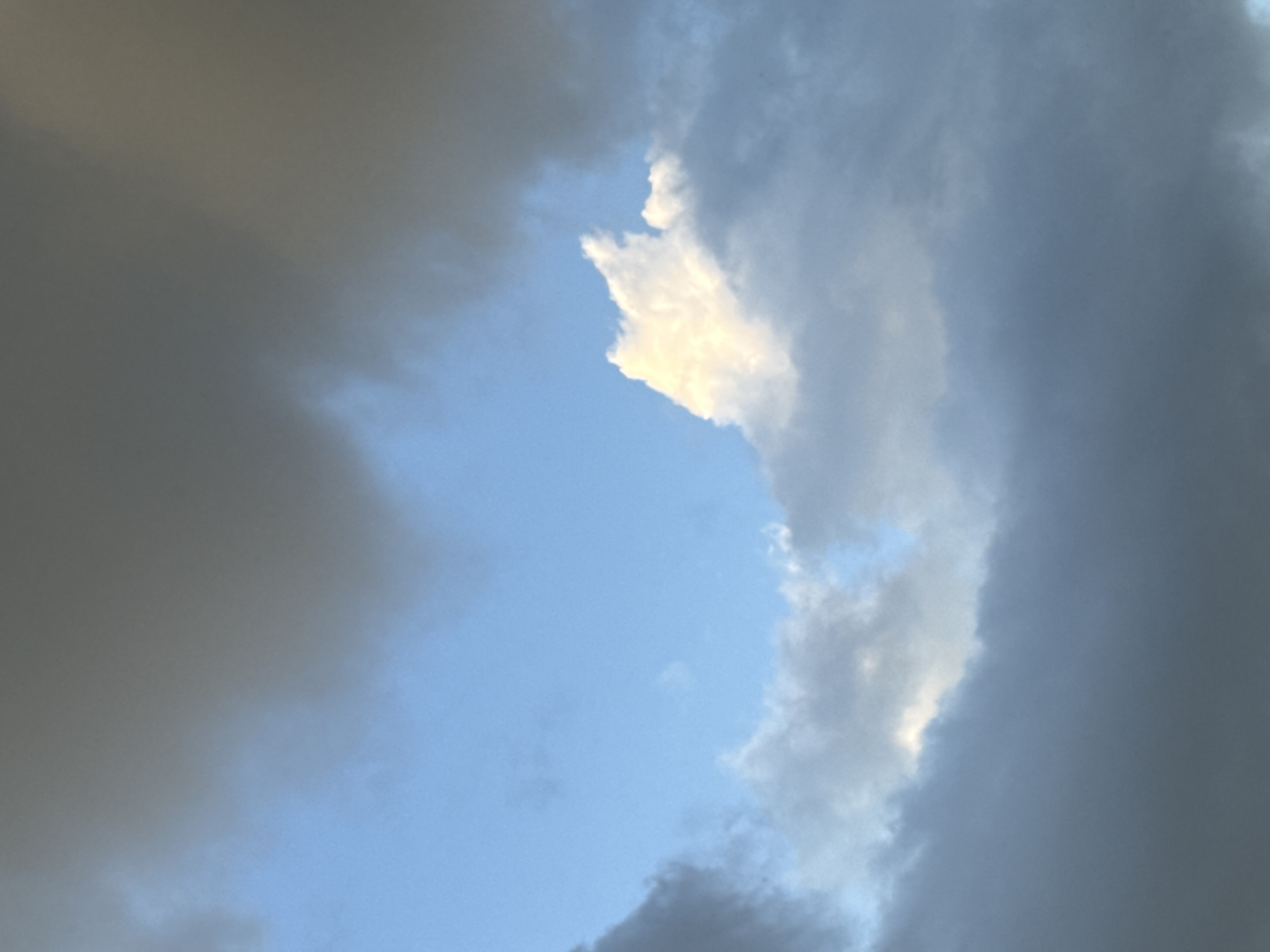 The image depicts a sky filled with clouds of varying shades of gray and white, with patches of blue sky visible. The lighting suggests it might be late afternoon or early evening. There are no discernible structures, people, or objects in the image, only clouds and sky. The location is stated as Voeikovo, Russia.