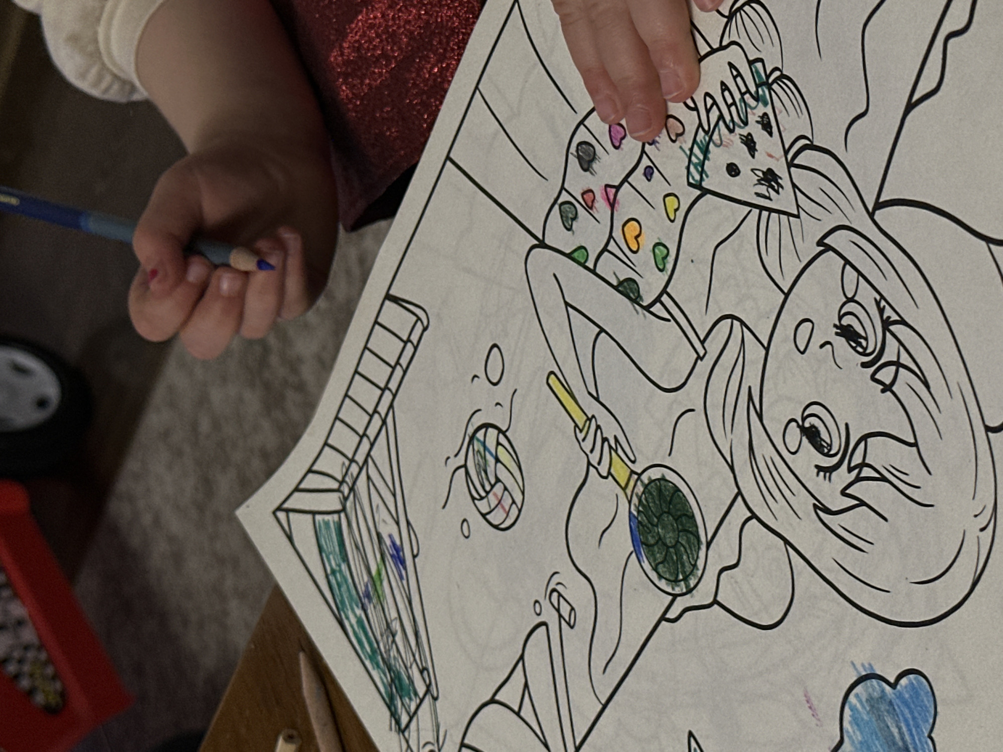A child is coloring a coloring page. The coloring page depicts a girl with long hair holding a pan, presumably in an indoor setting. The child is holding a blue colored pencil in their hand. The child has started coloring the page, using green, blue, yellow, red, and purple colors. It's not possible to locate the city of Tbilisi, Georgia from this image.