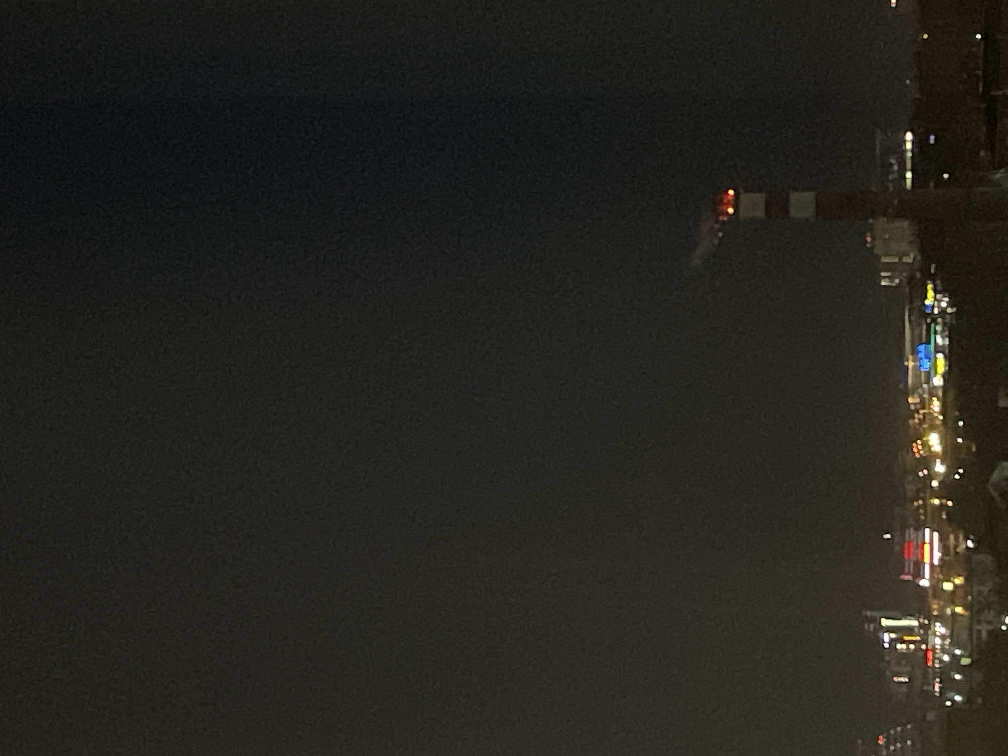 At night, the image presents a view of a city skyline, possibly Izhevsk, Russia, with prominent light patterns indicating urban development. To the right, city lights illuminate buildings and streets. In the distance, a construction crane stands out against the night sky, marked by its warning lights on top. The sky above is dark, contrasting with the urban glow. The image predominantly shows the urban environment.