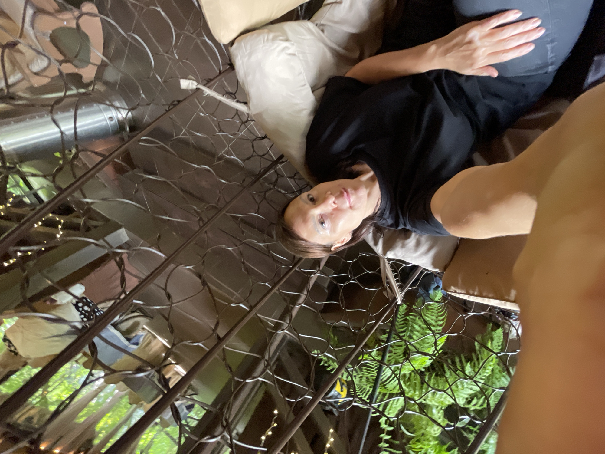 A woman is lying on cushioned furniture in a lattice-enclosed space. The view outside the lattice reveals vegetation, suggesting an outdoor setting. The image appears to be taken from a low angle. The location is Solokh-Aul, Russia.